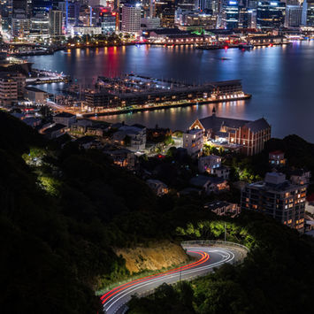 Wellington central business area and waterfront lit up at night with a light trail on the road as taken from a point up Mt Victoria.