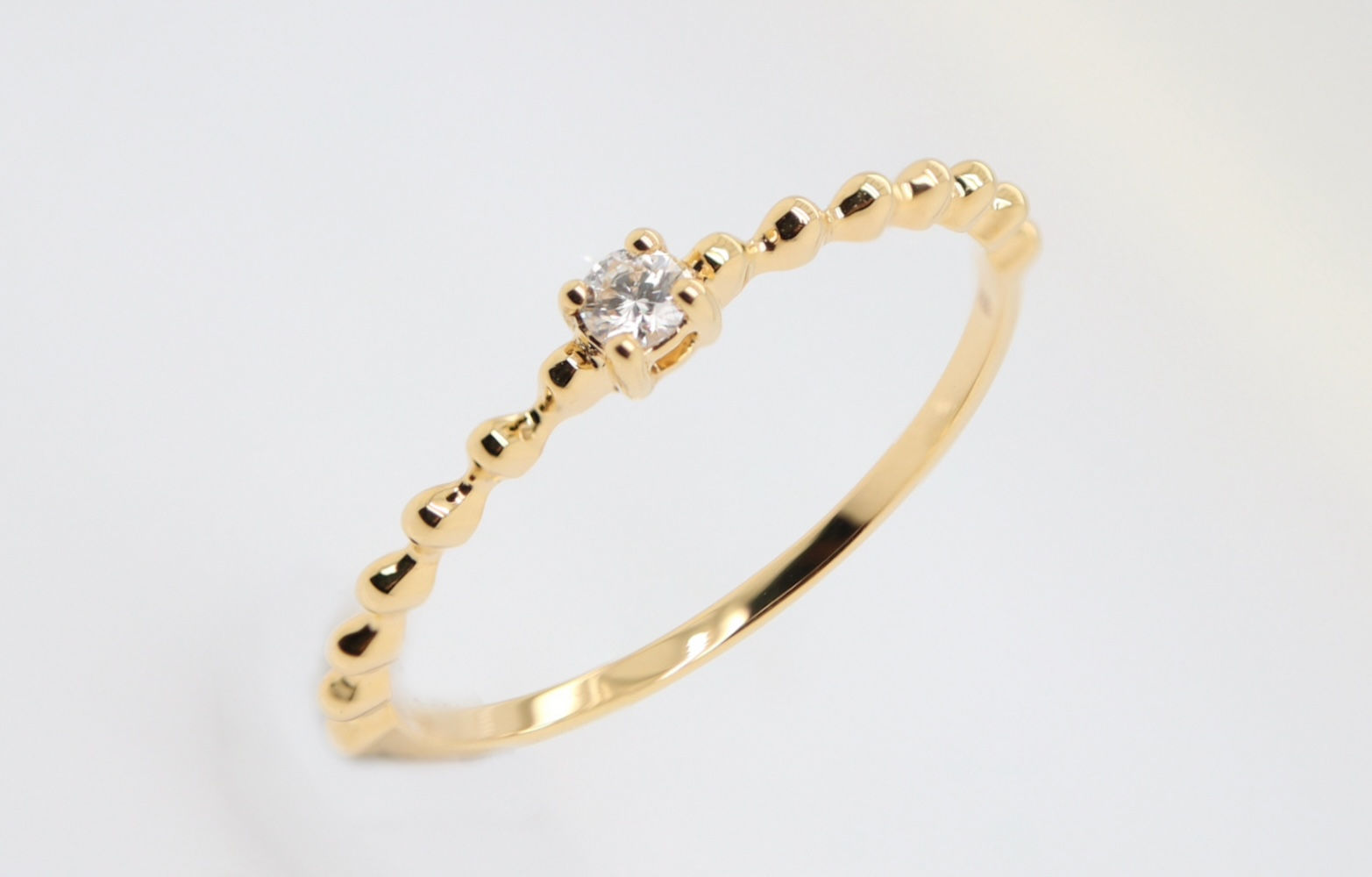 Dainty diamond ring with a single brilliant stone on a delicate beaded gold stacking band.