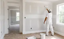 Contractor painting freshly installed drywall during home reconstruction after water damage