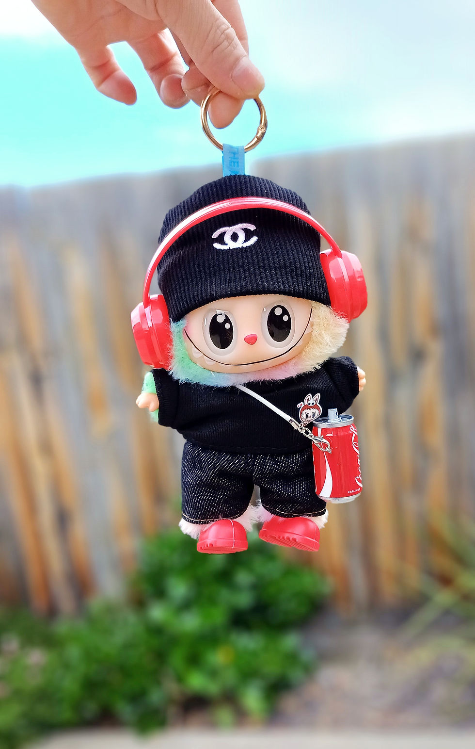 front view labubu wearing a black outfit with red headphone and coke charm.