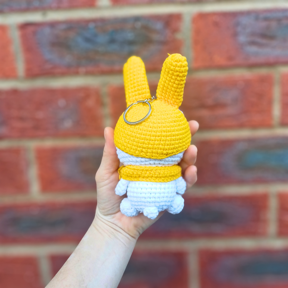 Thumbnail: Back view of a handmade yellow bunny amigurumi keychain with long ears and knitted scarf.