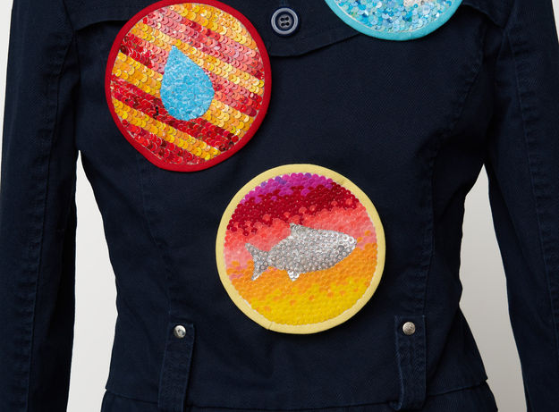 an artwork made of a jacket with pinned on patches decorated with repurposed plastic sequins