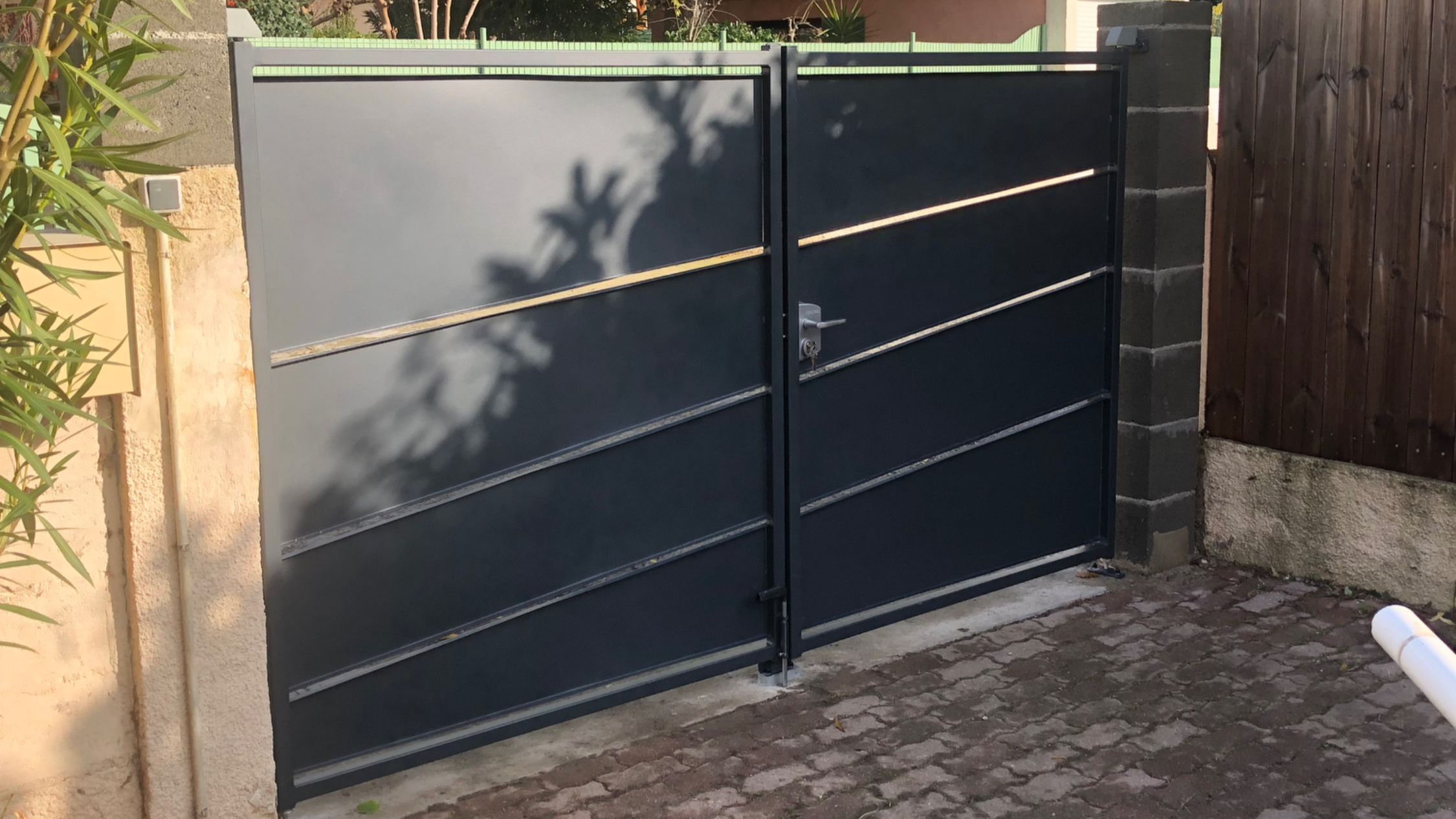 Portail sombre avec lignes diagonales, devant une allée pavée, près des arbres.