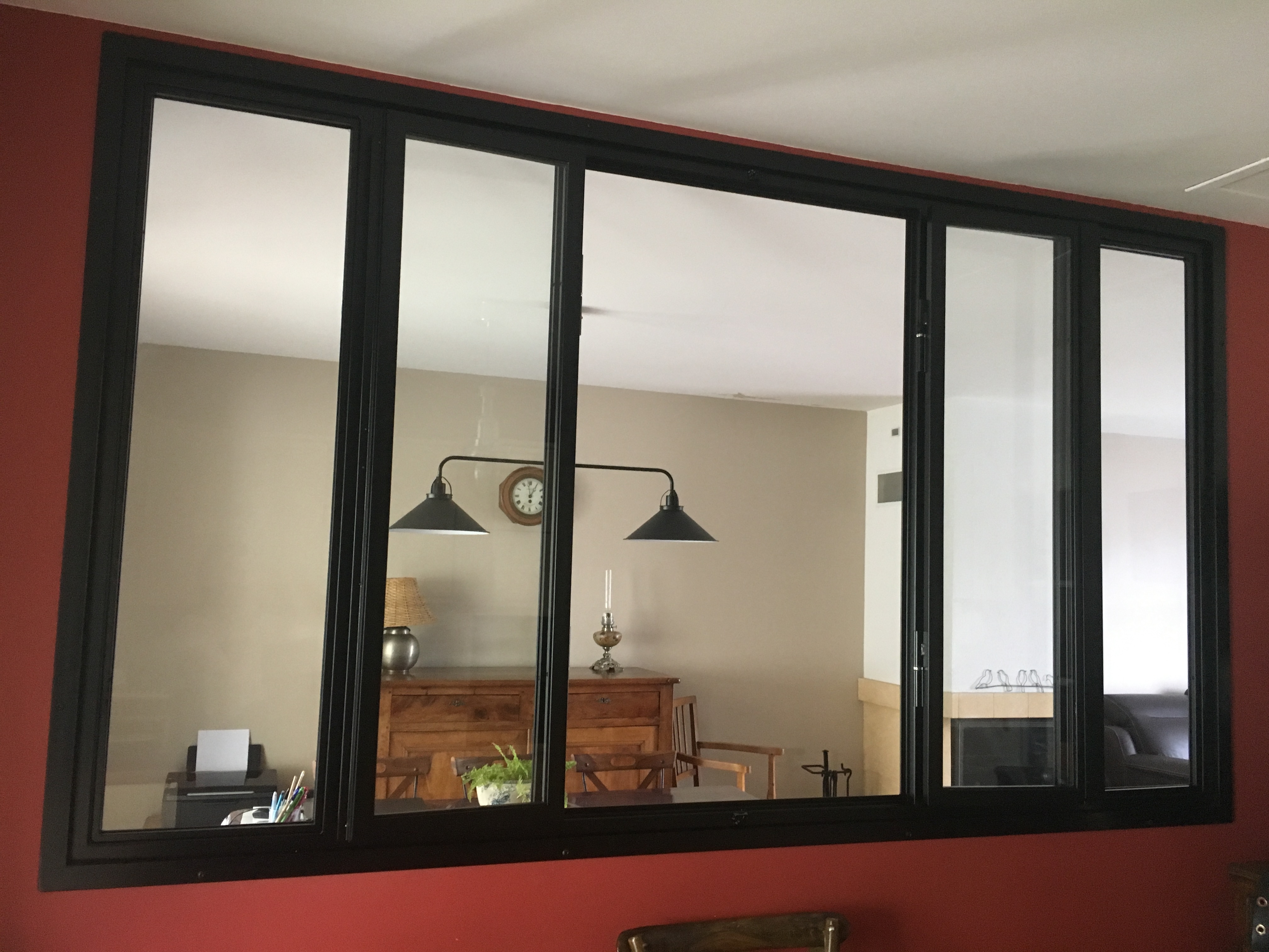 Grande fenêtre noire avec reflets du salon, éclairage, table et objets décoratifs.