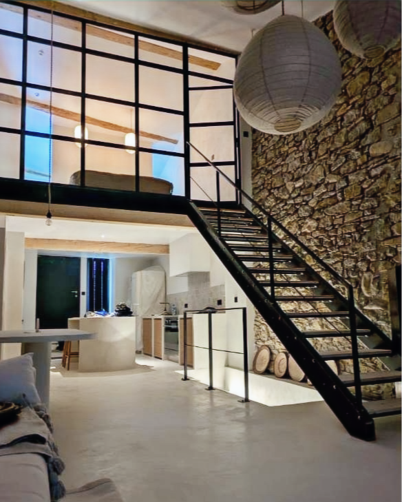 Intérieur moderne avec escalier en fer, mur en pierre, luminaire, et mezzanine.