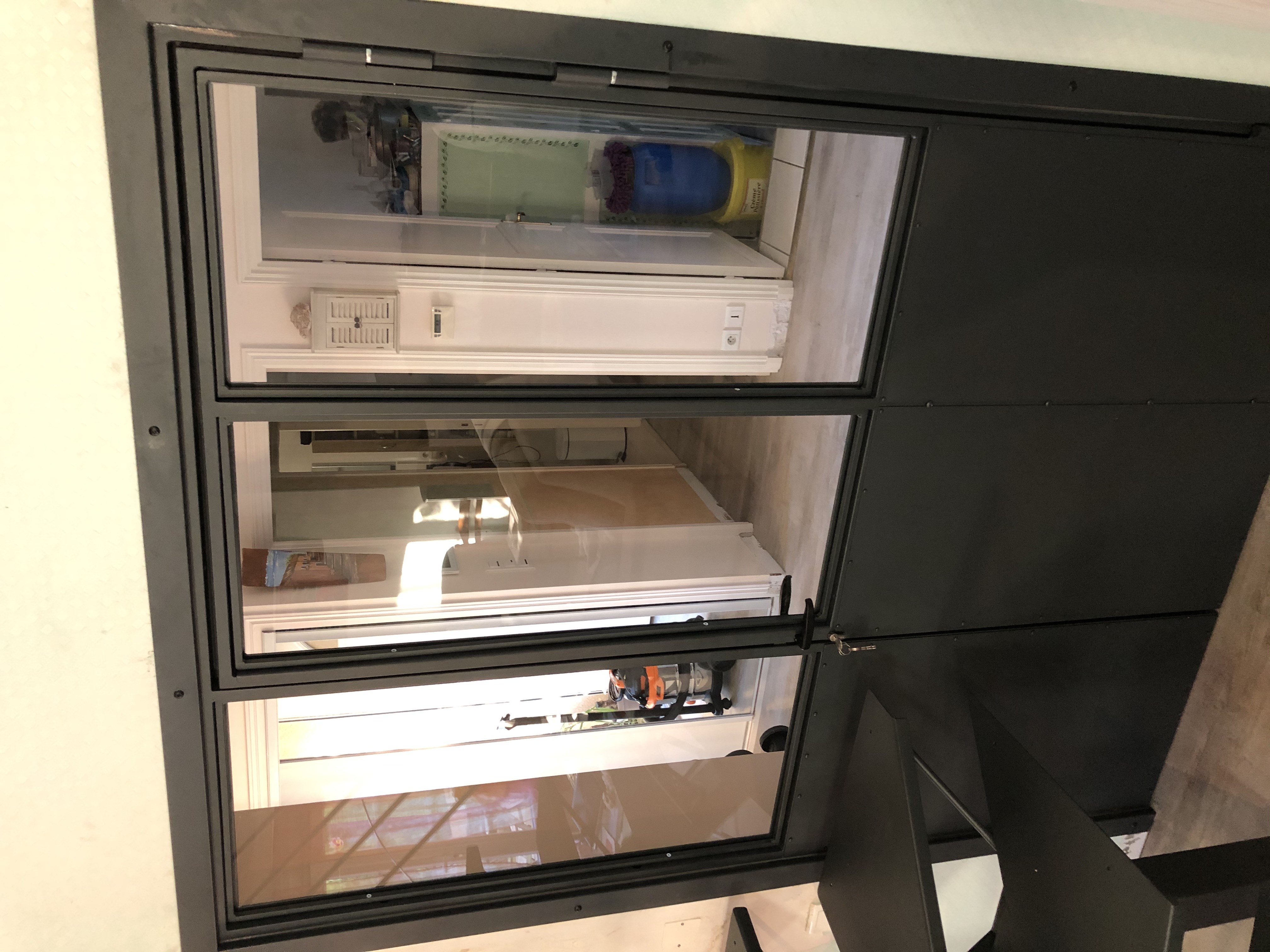 Verrière noire avec trois panneaux de verre, vue vers un intérieur clair.