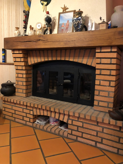 Cheminée en briques, avec un insert noir métalique et des ornements décoratifs, sous un manteau.