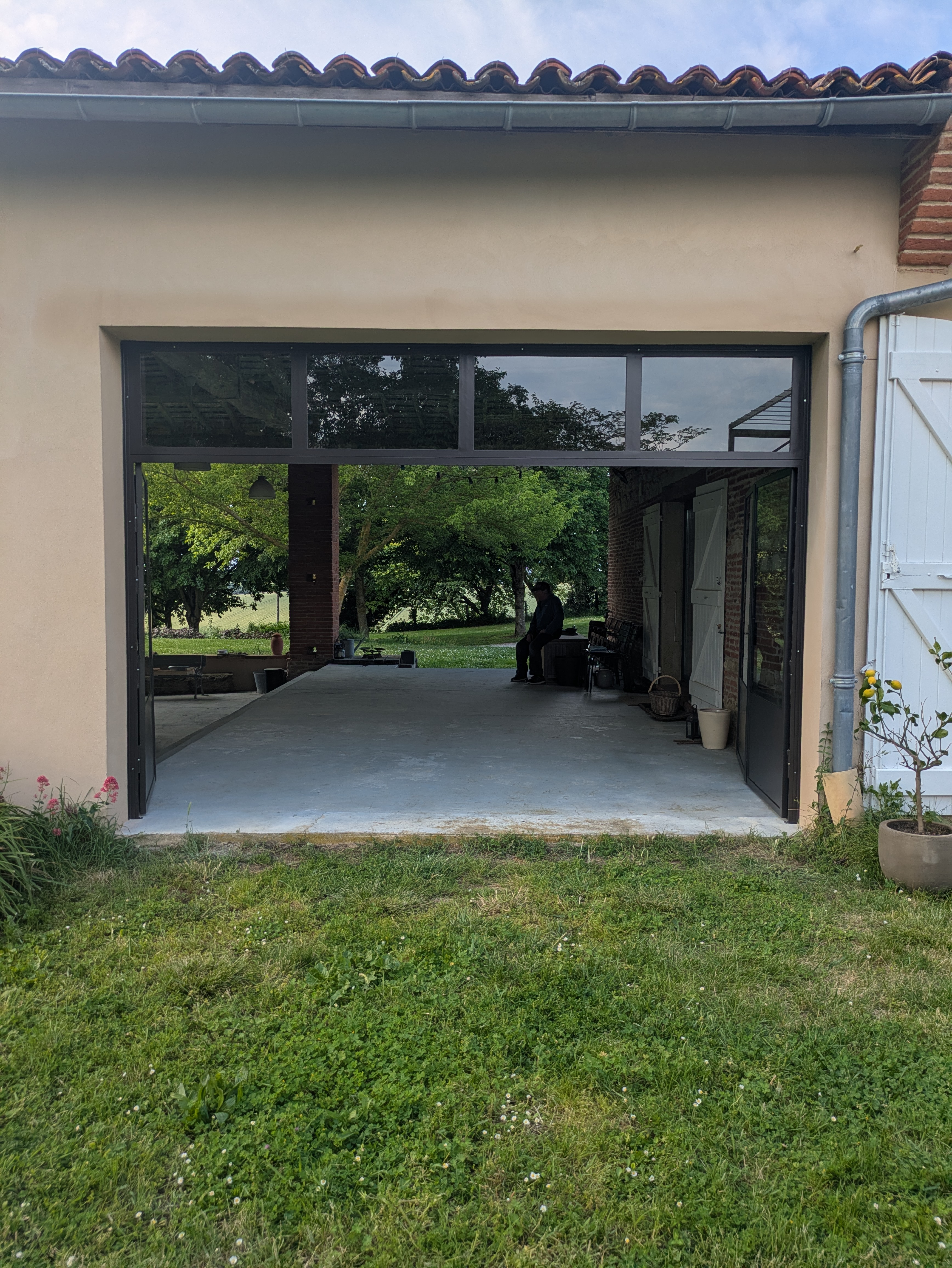 Garage ouvert avec vue sur l'extérieur, reflet des arbres, béton et herbe.