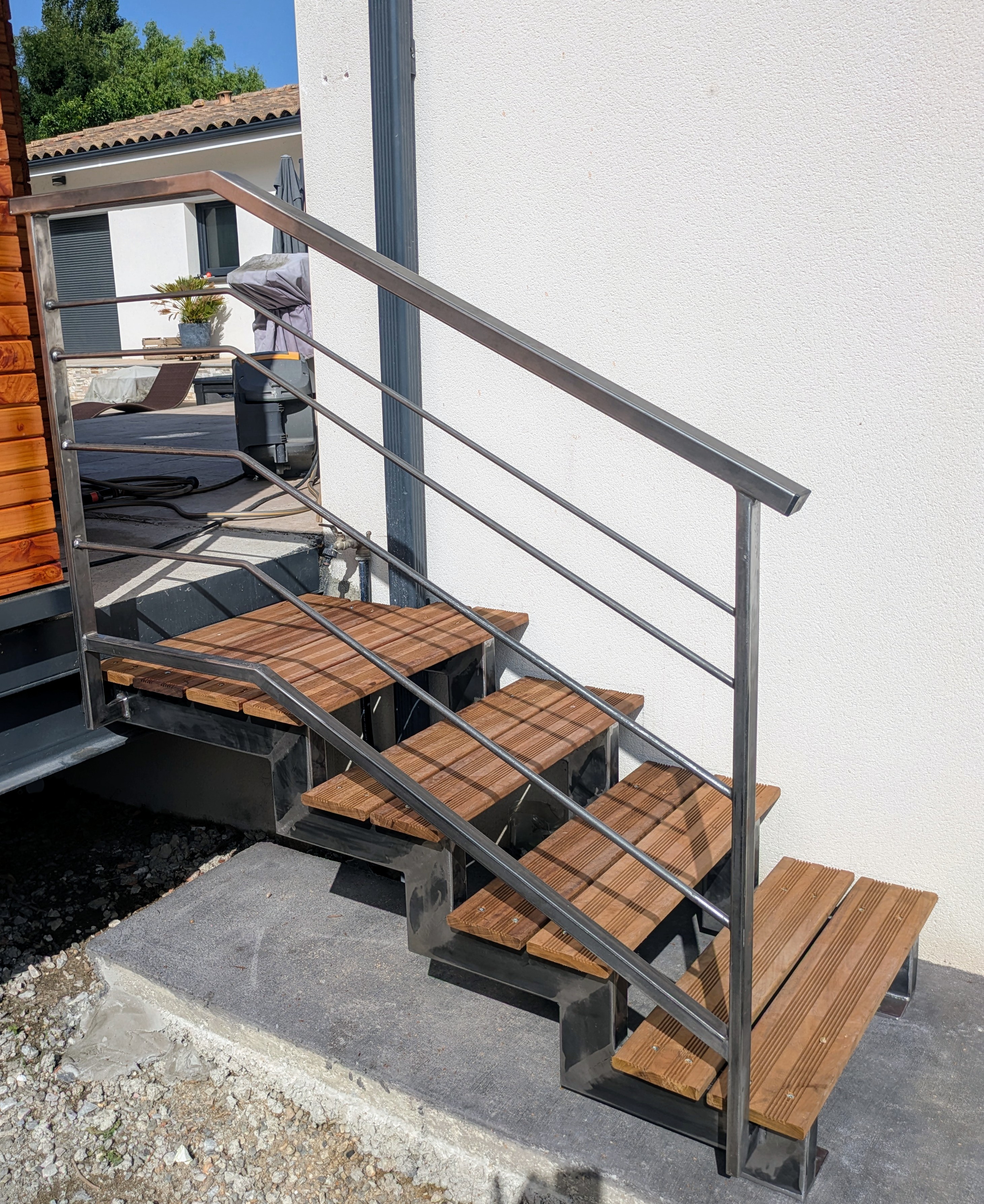 Escalier extérieur avec marches en bois, rampe métallique et espace extérieur.