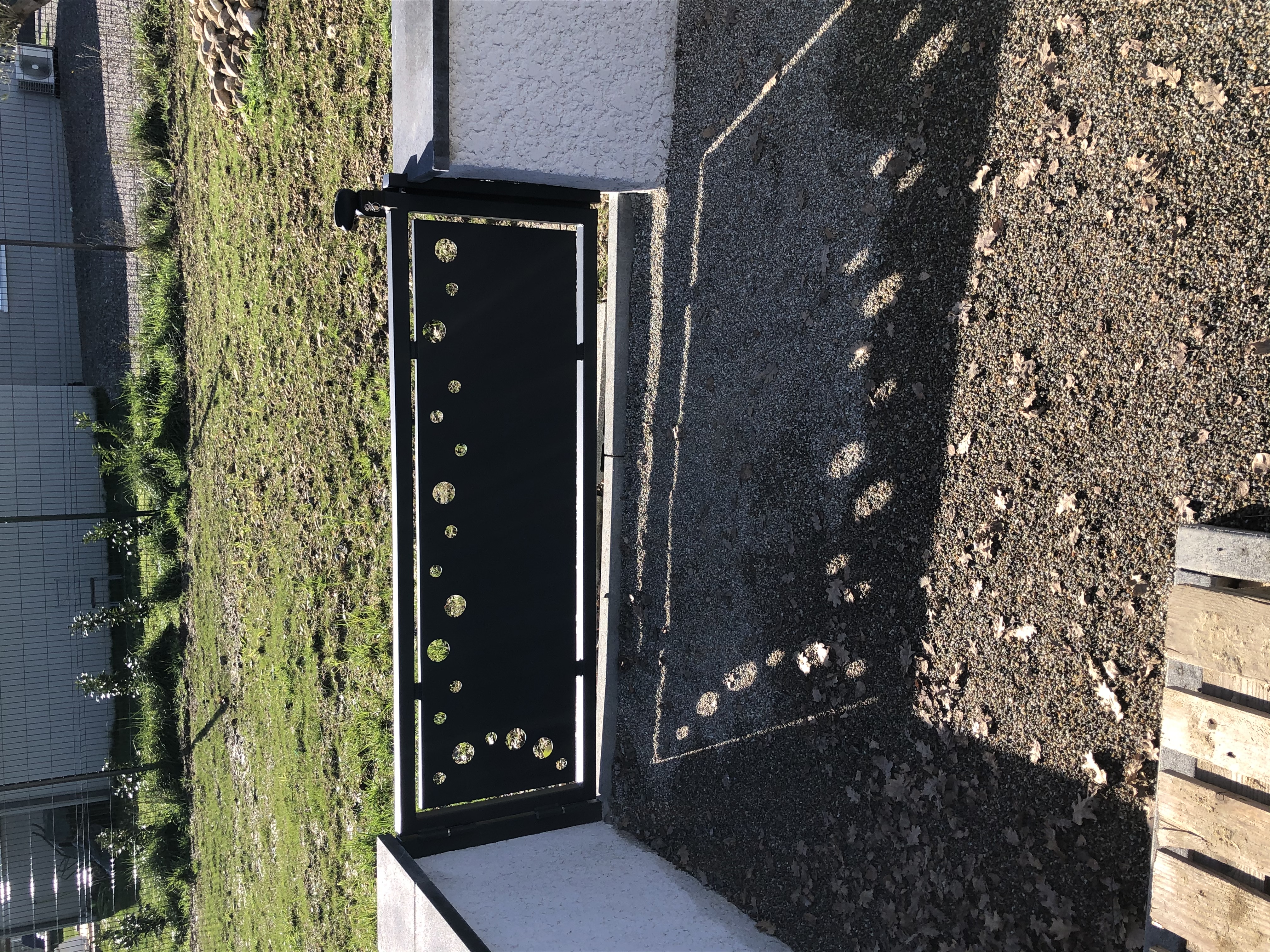 Un portail noir décoré de motifs ronds devant le jardin avec un mur.