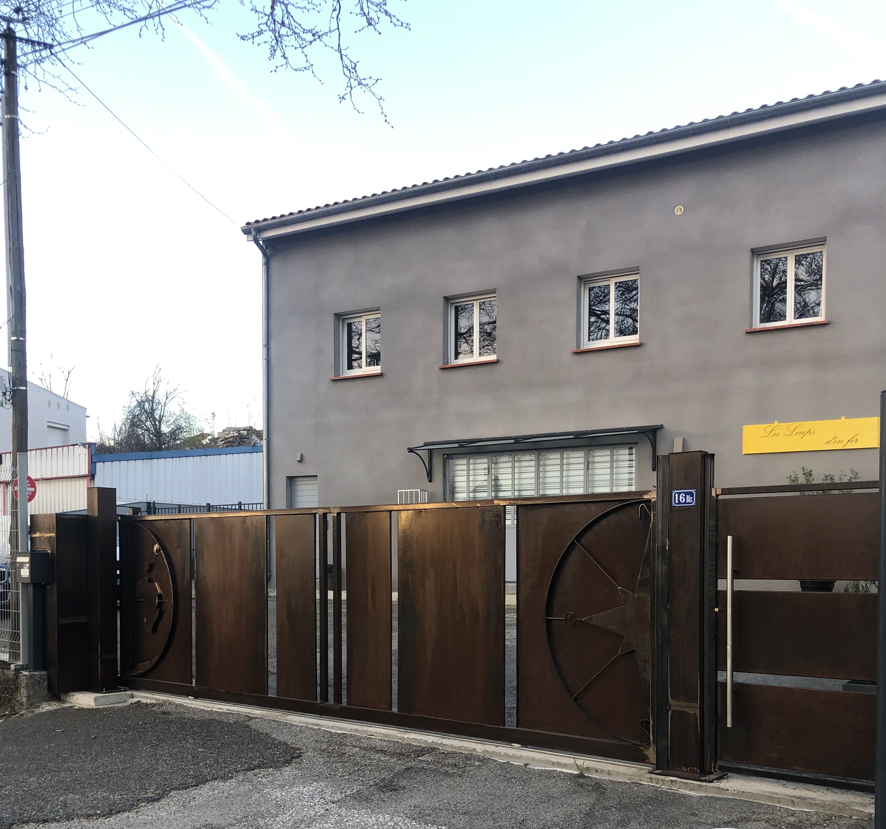 Grand portail en métal rouillé devant un bâtiment gris, porte fermée, Christo.