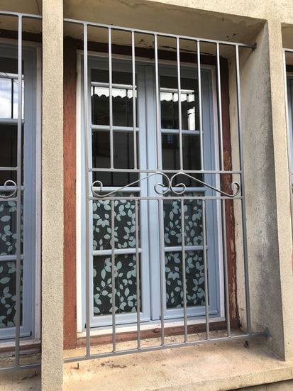 Fenêtre grise avec grille de sécurité, avec rideaux à motifs floraux.