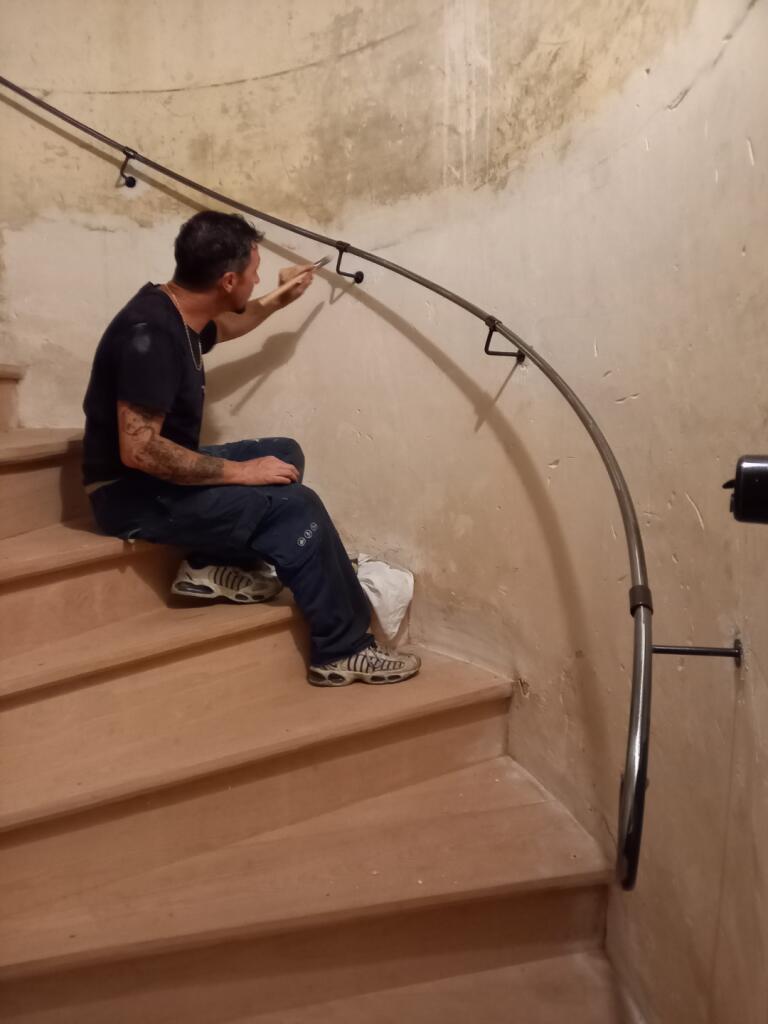 Homme assis sur un escalier, tenant un objet près de la rampe Escalier & Rampe