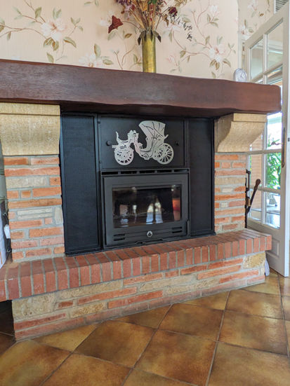 Cheminée en briques, avec un insert noir métalique et des ornements décoratifs, sous un manteau.