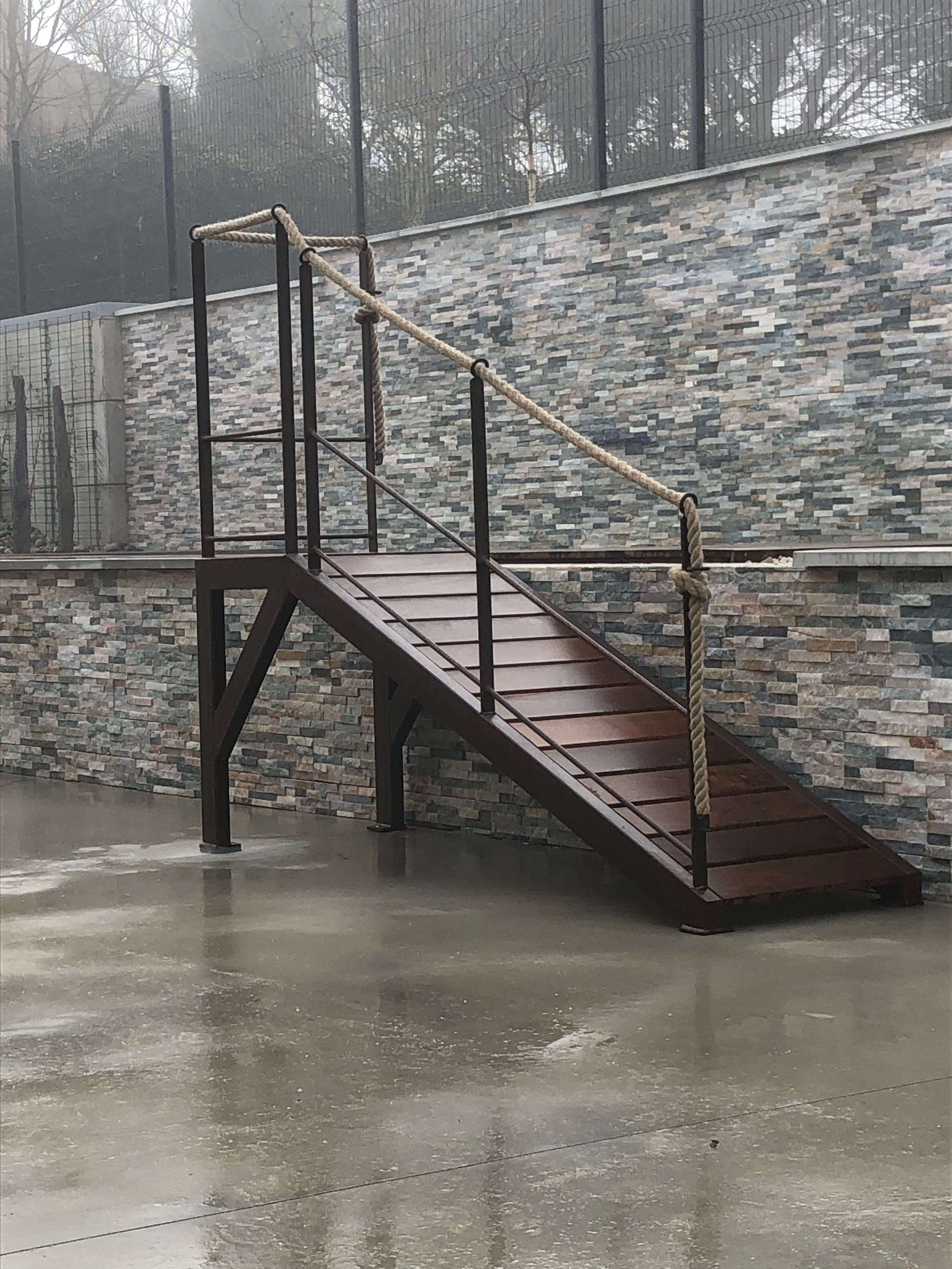 Marches en bois et Escalier & Rampe sur fond de mur en pierre, journée pluvieuse.