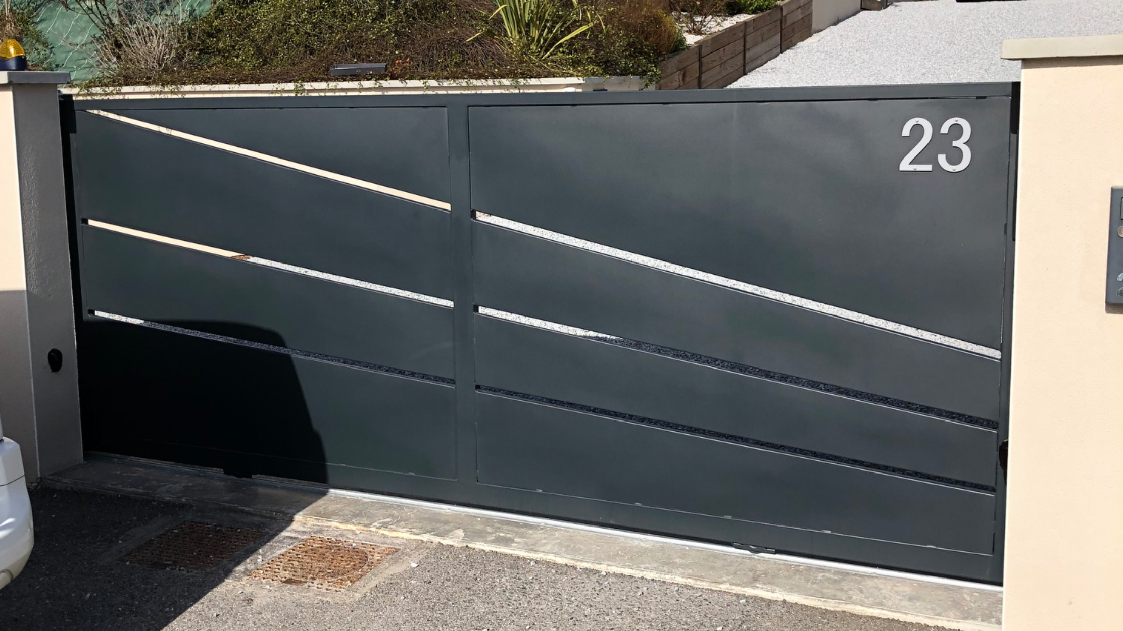 Portail gris avec numéro 23 devant une maison arborée et voiture.