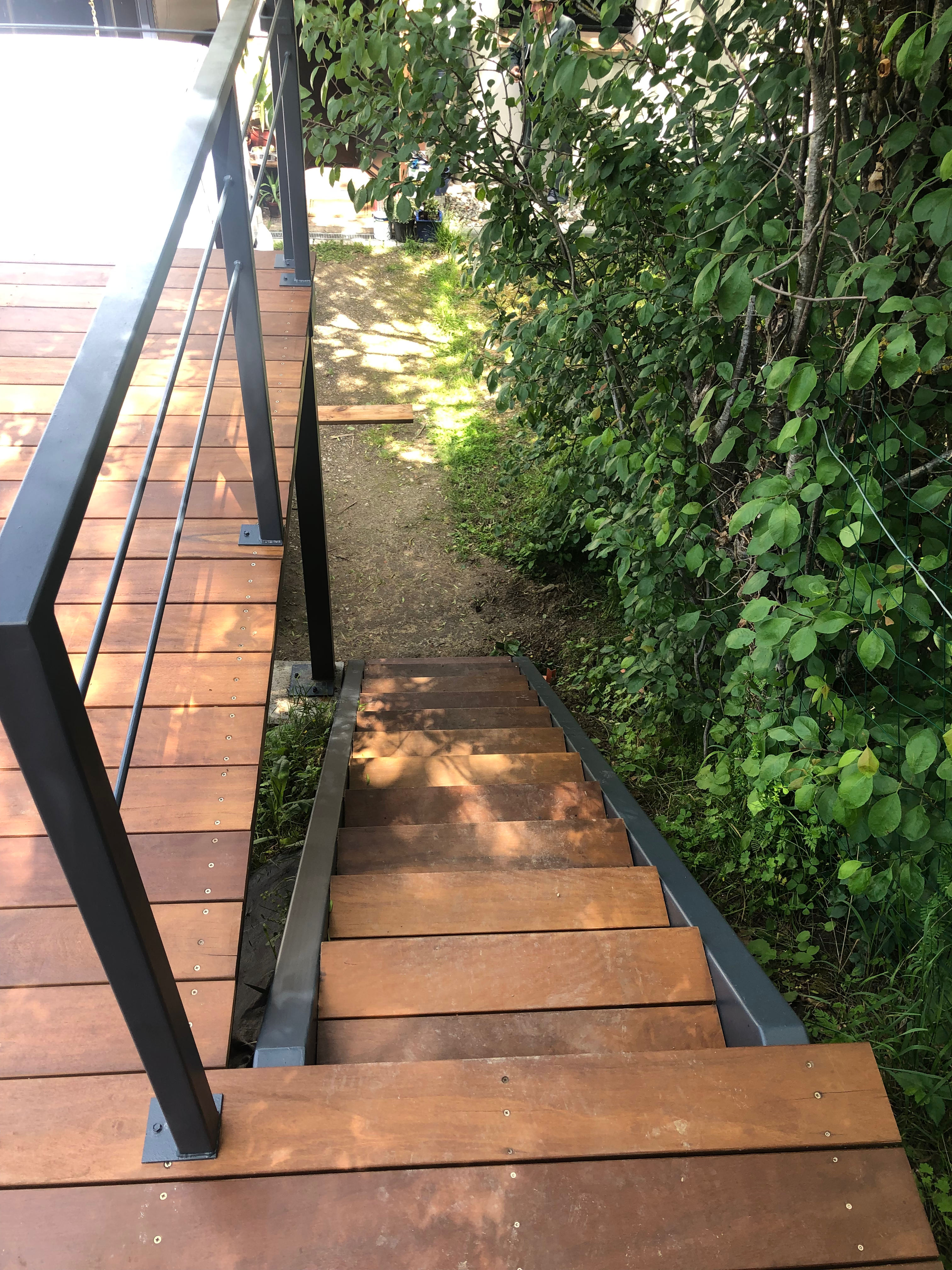 Escalier en bois menant au jardin, avec rampe métallique et verdure environnante.