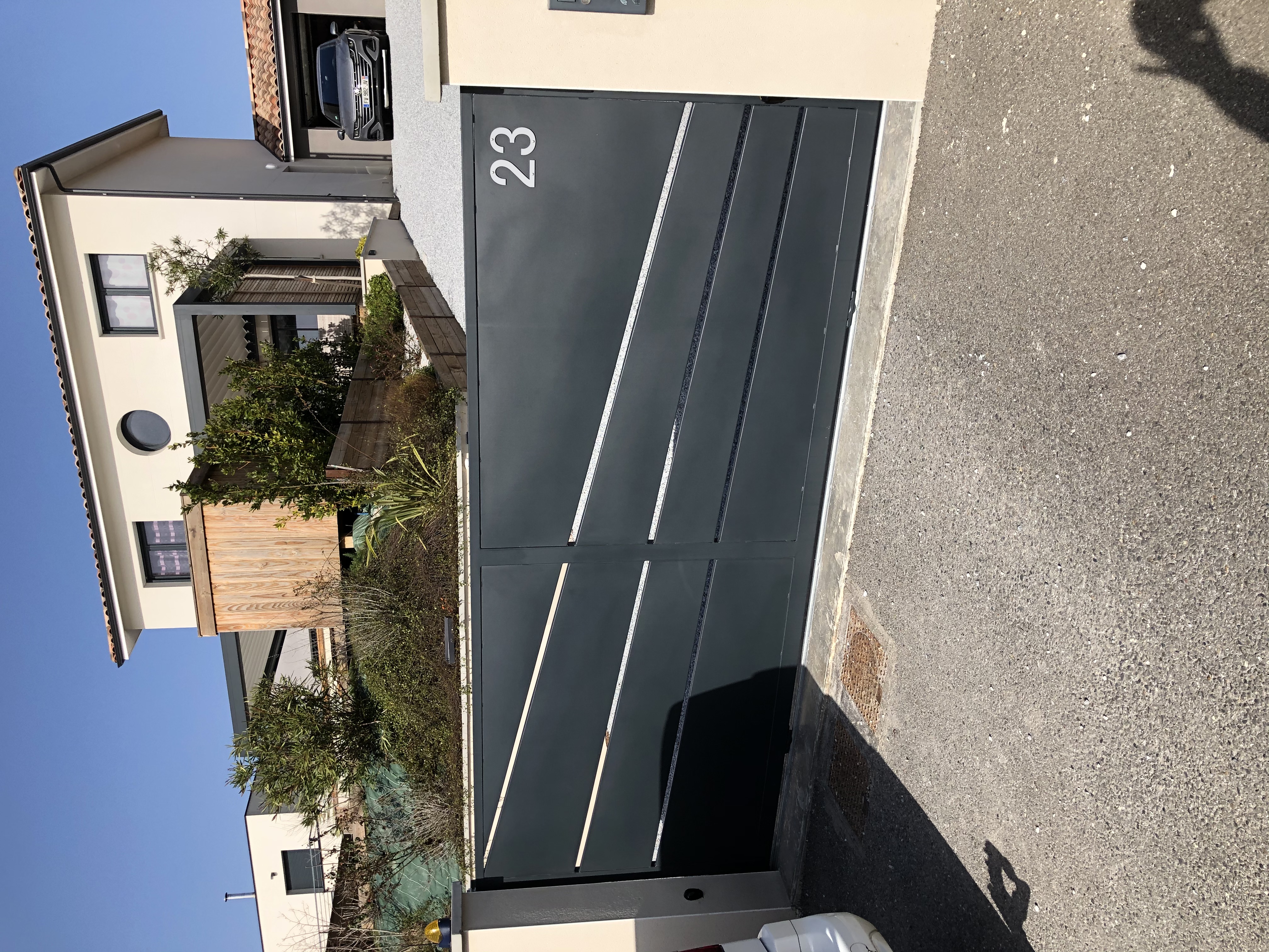 Portail gris avec numéro 23 devant une maison arborée et voiture.