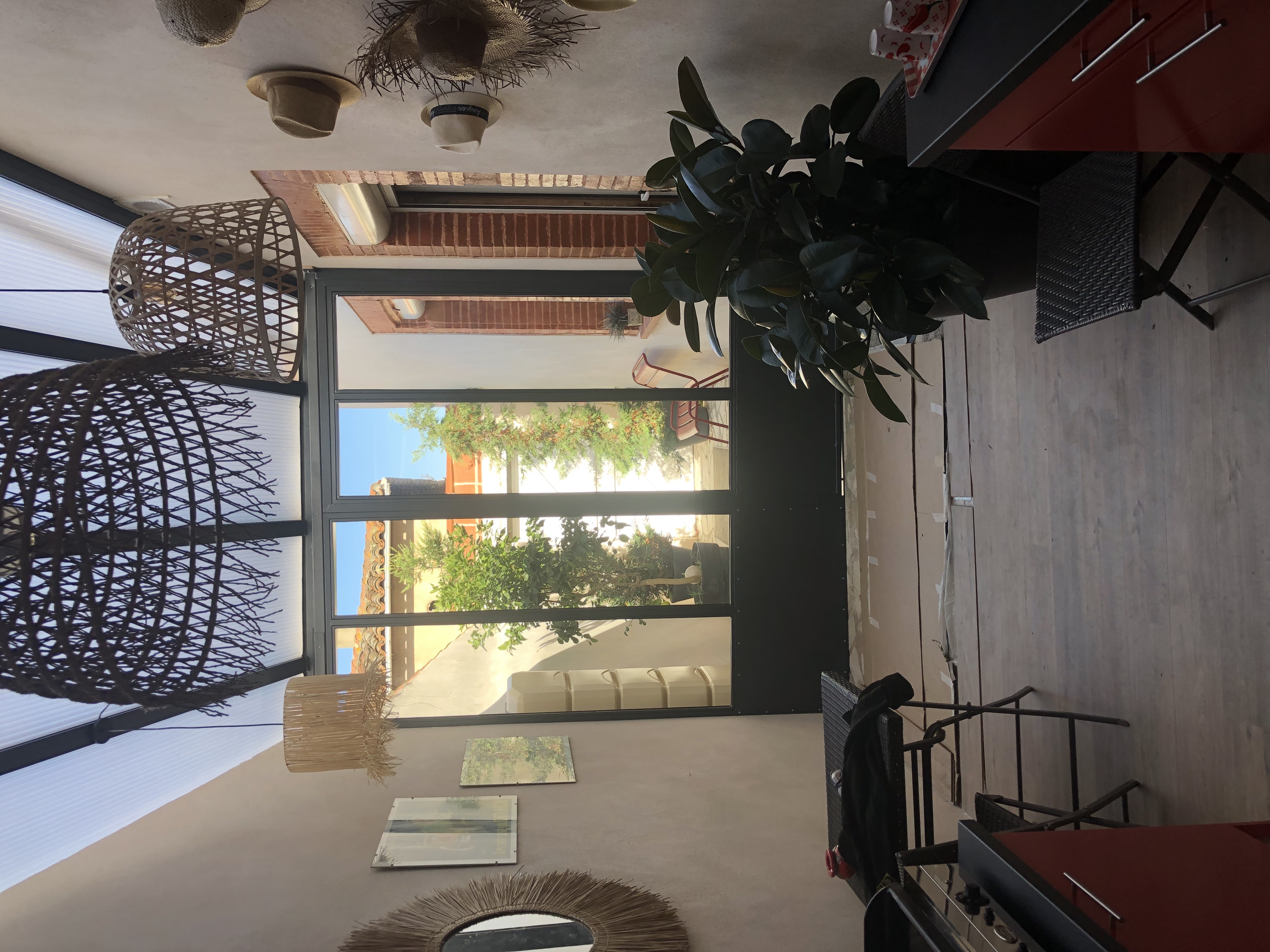 Intérieur avec porte vitrée, miroirs et plantes, sous une verrière. Lumineux et accueillant espace.