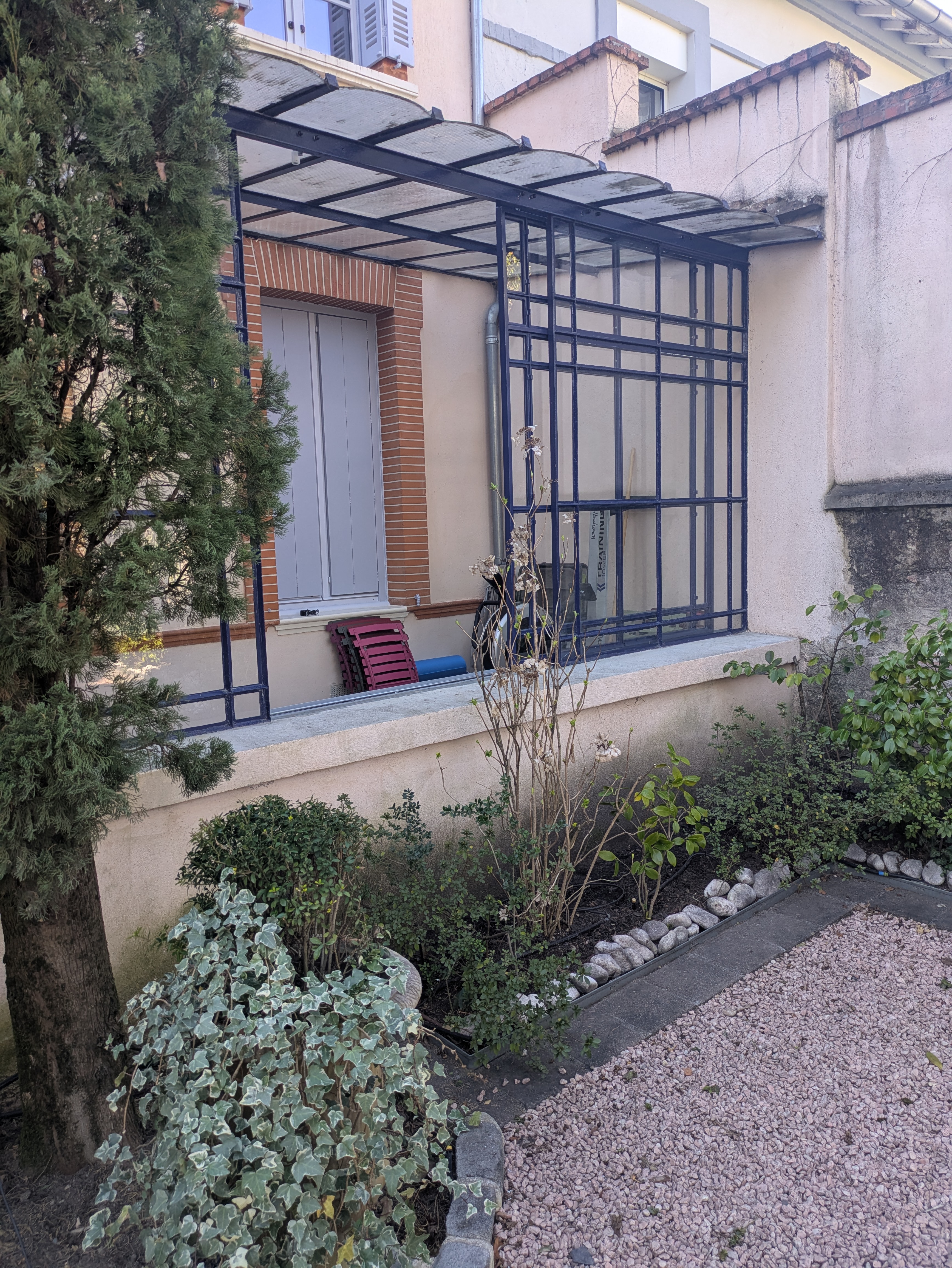 Une verrière métallique avec une fenêtre et des plantes; extérieur d'une maison.