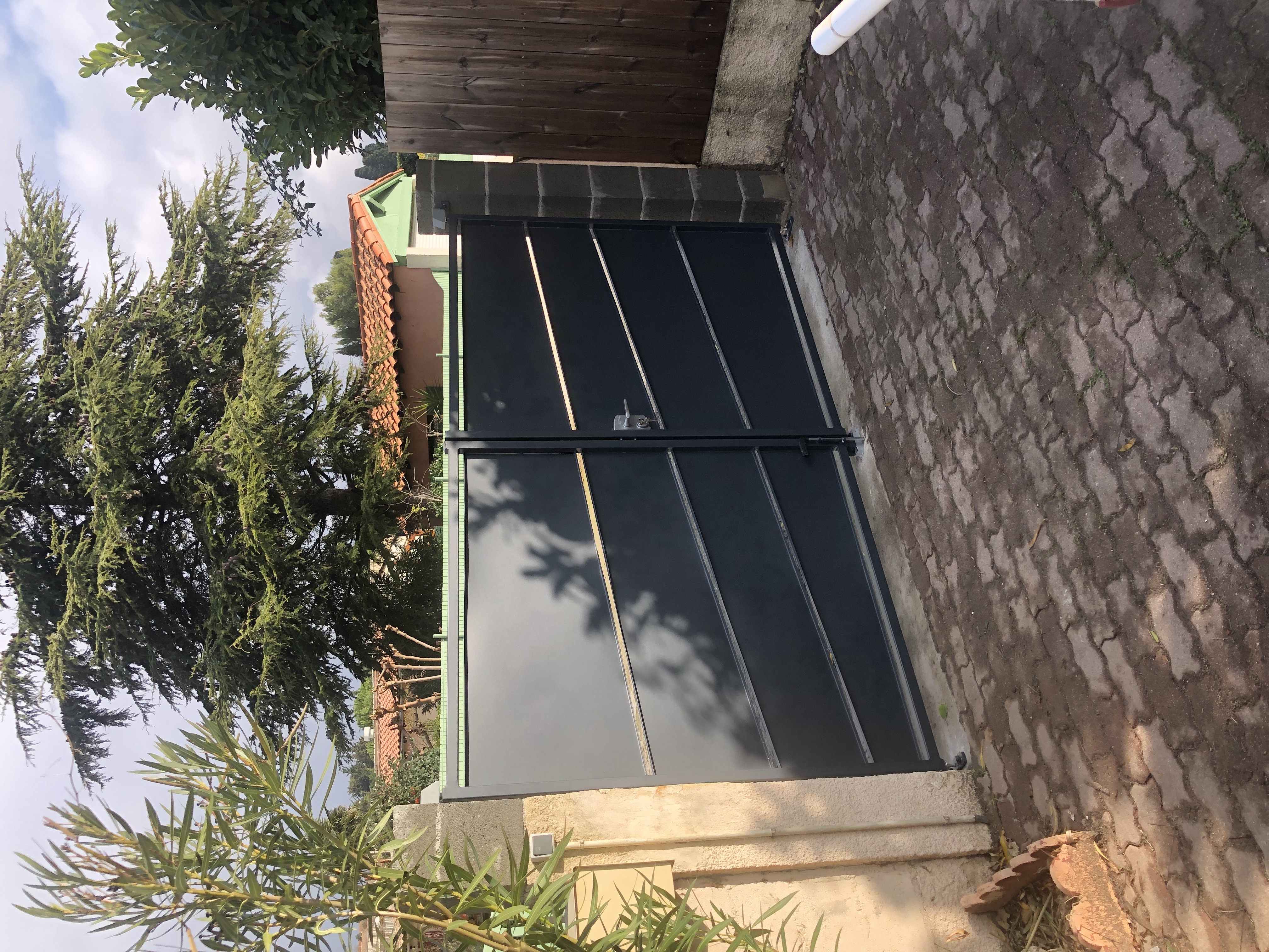 Portail sombre avec lignes diagonales, devant une allée pavée, près des arbres.