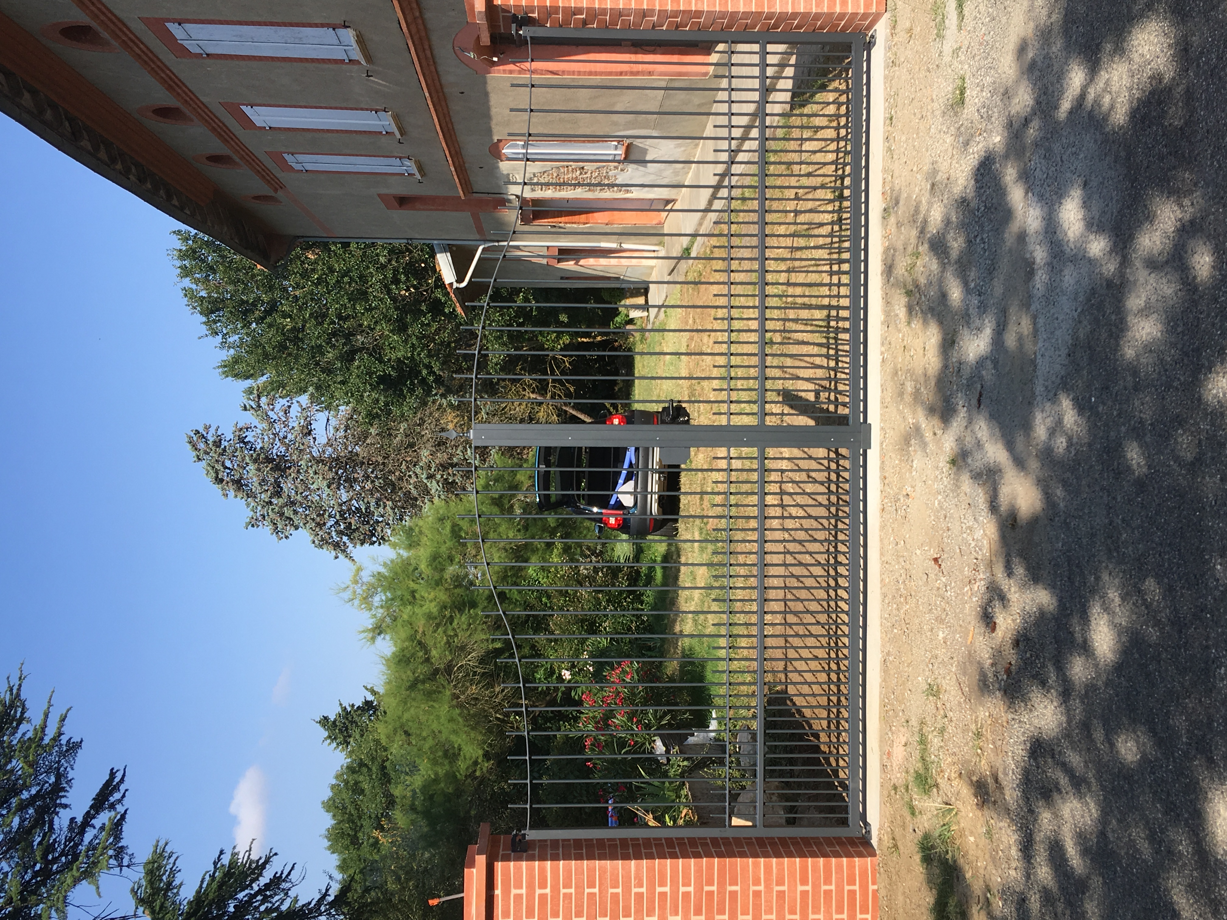 Portail en fer devant une maison avec une voiture garée. Christo.