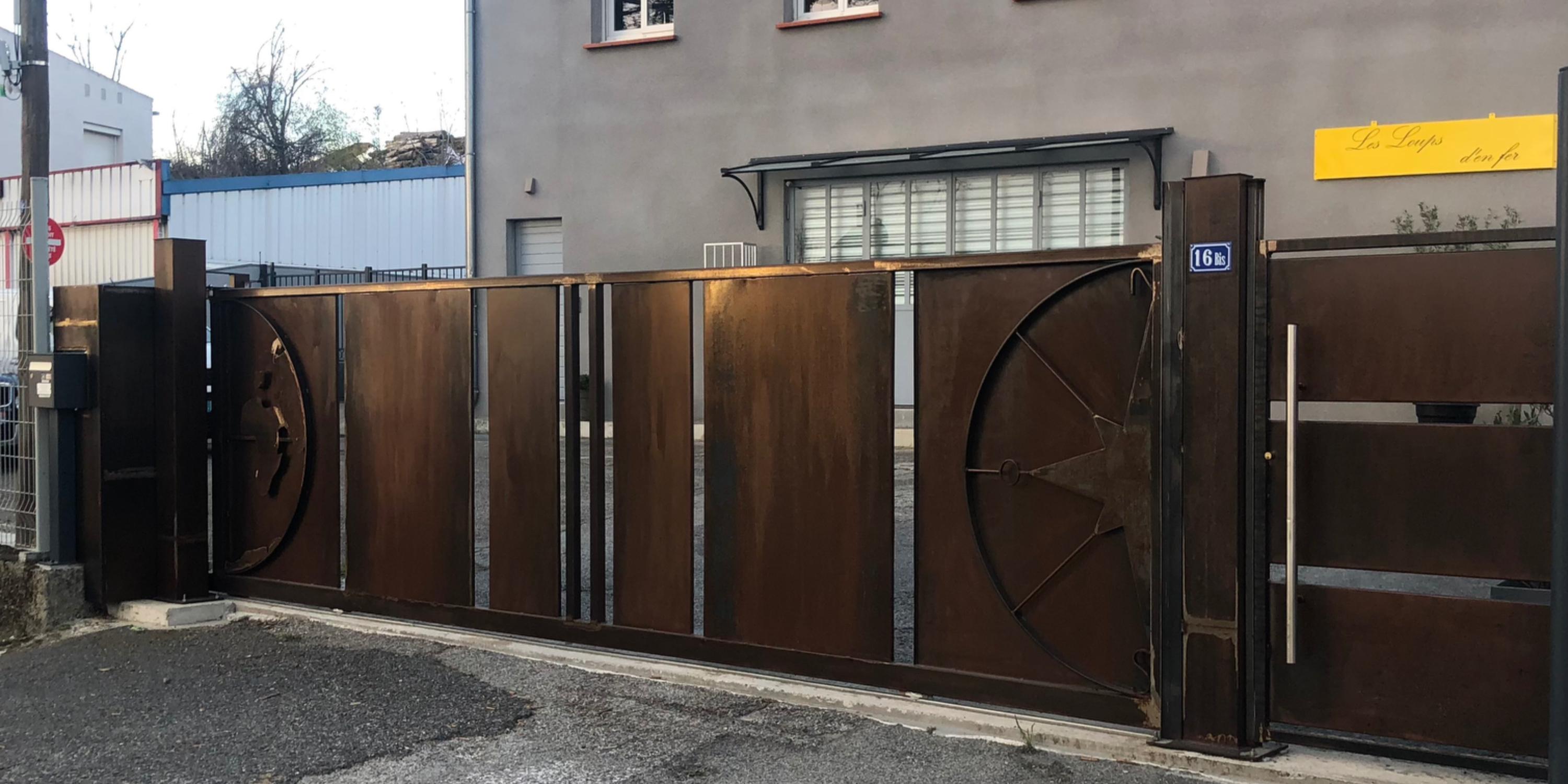 Grand portail en métal rouillé devant un bâtiment gris, porte fermée, Christo.