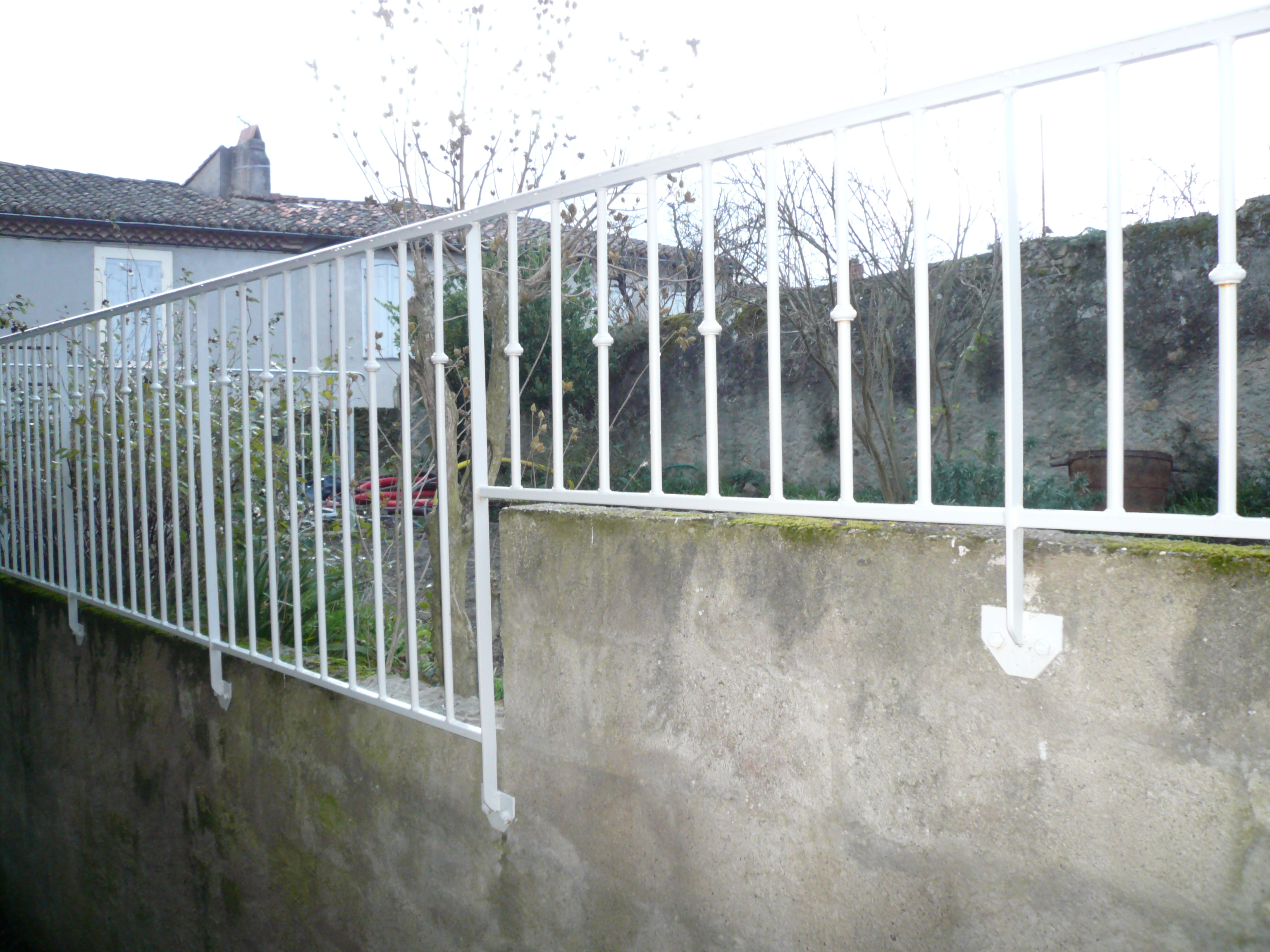 Barrière blanche en métal, Escalier & Rampe, devant un mur en béton et maison.