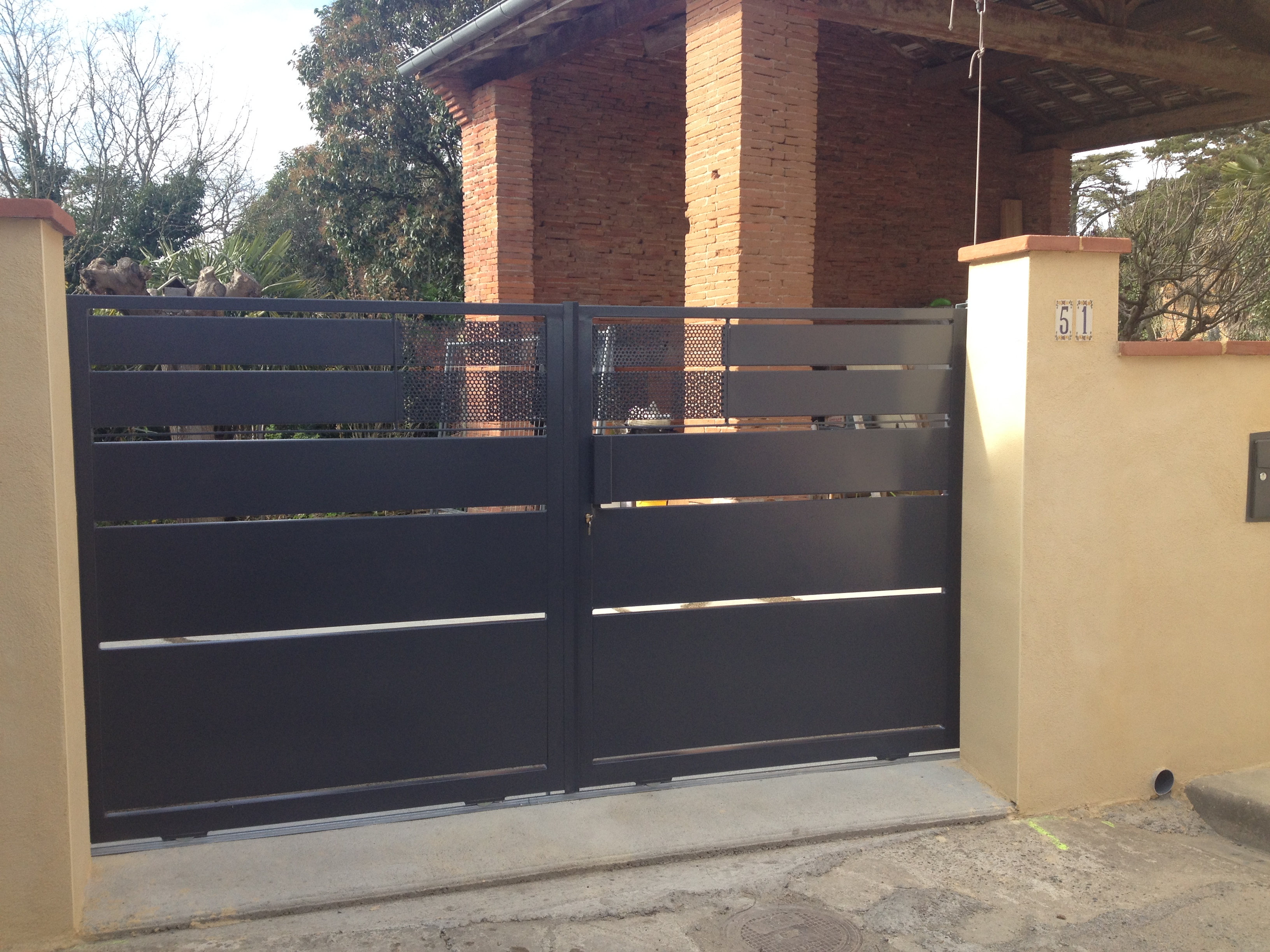 Portail métallique fermé, portes grises. Bâtiment en briques rouges en arrière-plan.