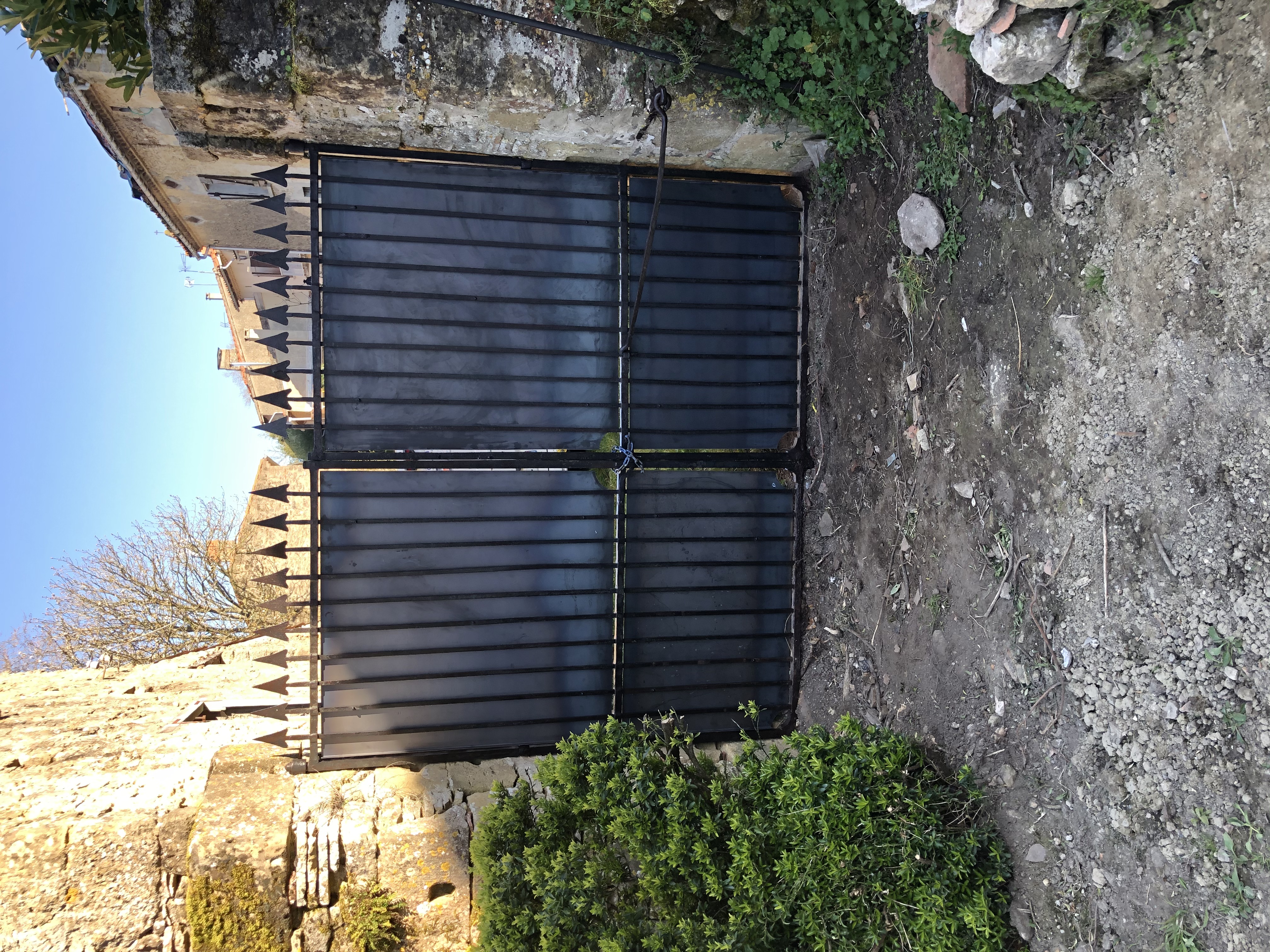 Grandes portes noires en fer forgé gardant l'entrée. Portail devant vieux murs.