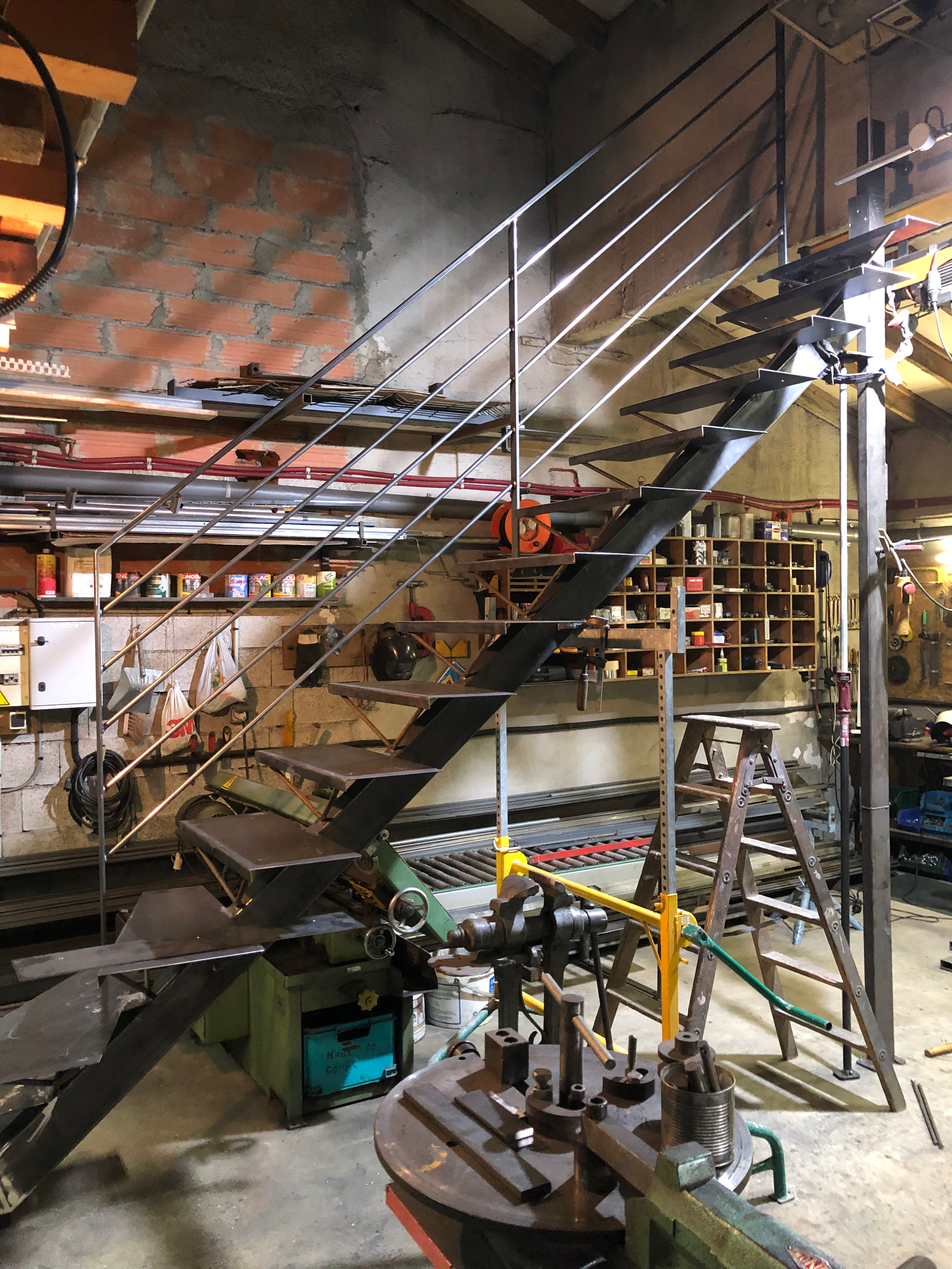 Escalier métallique dans un atelier, avec rampe, en arrière-plan des outils industriels.