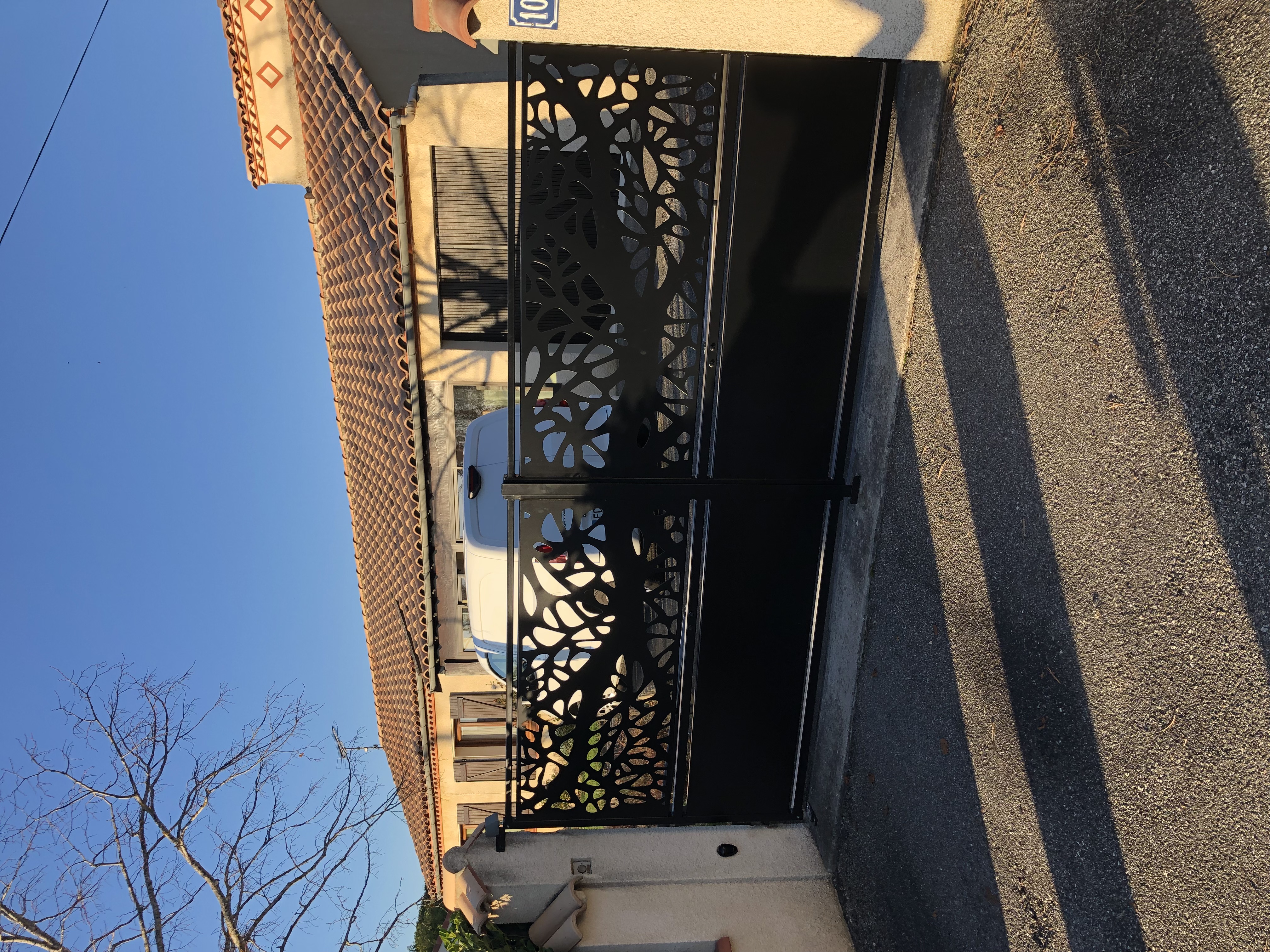 Portail noir orné de motifs, devant une maison vue en journée avec Christo.