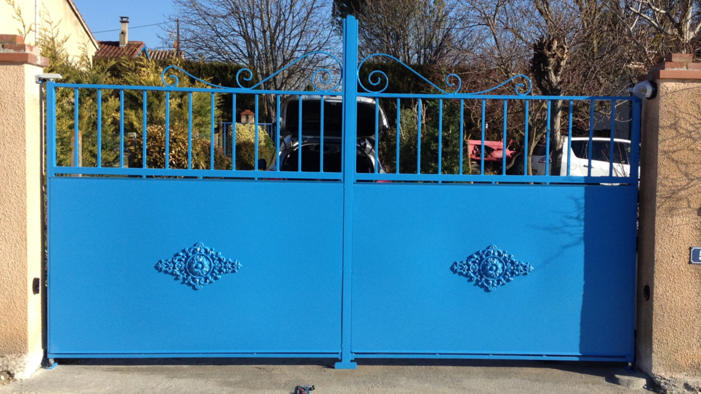 Portail bleu fermé devant une maison. Décorations et texte avec numéro.