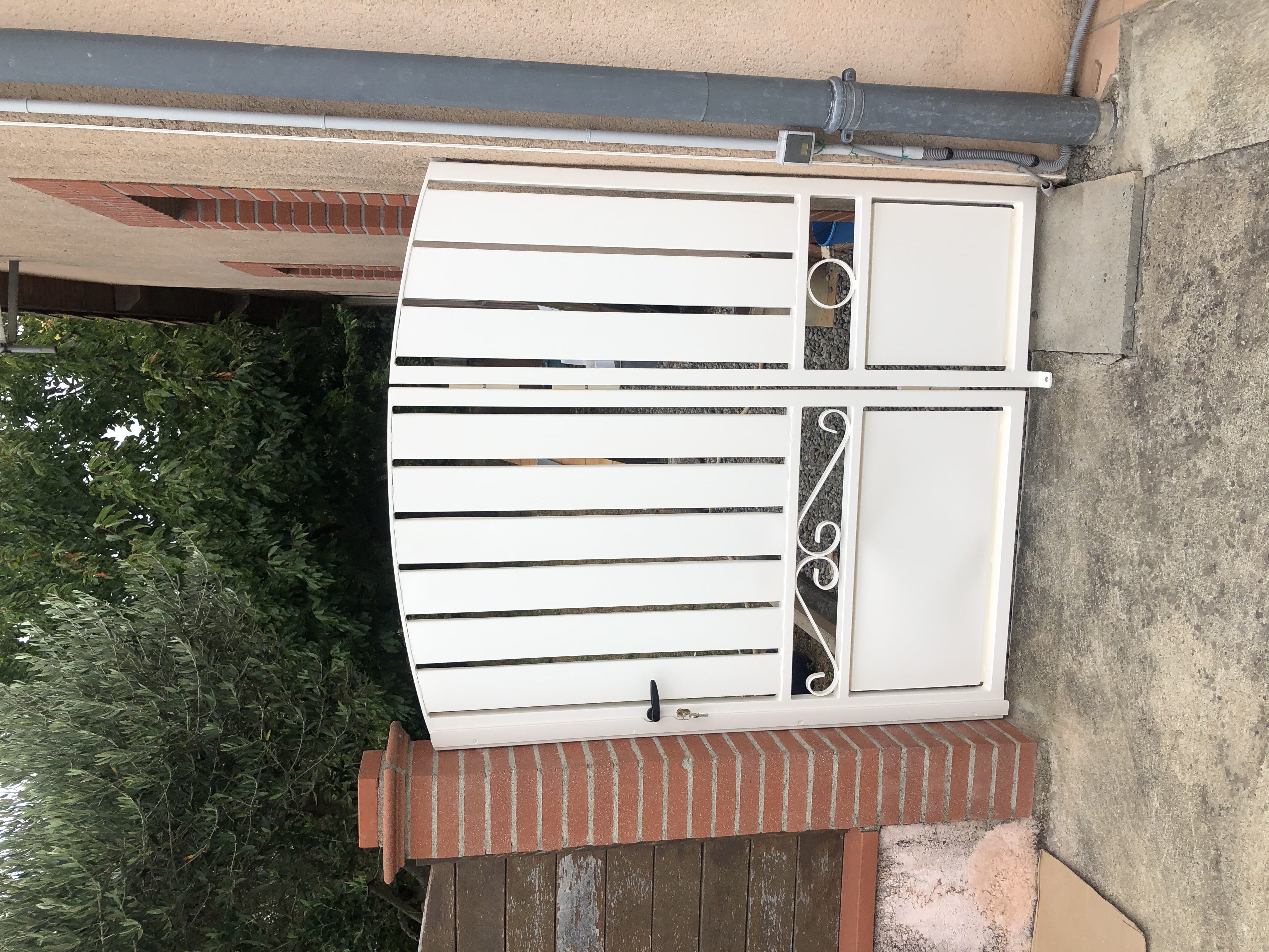 Portail blanc fermé devant une maison, avec des détails en fer forgé.