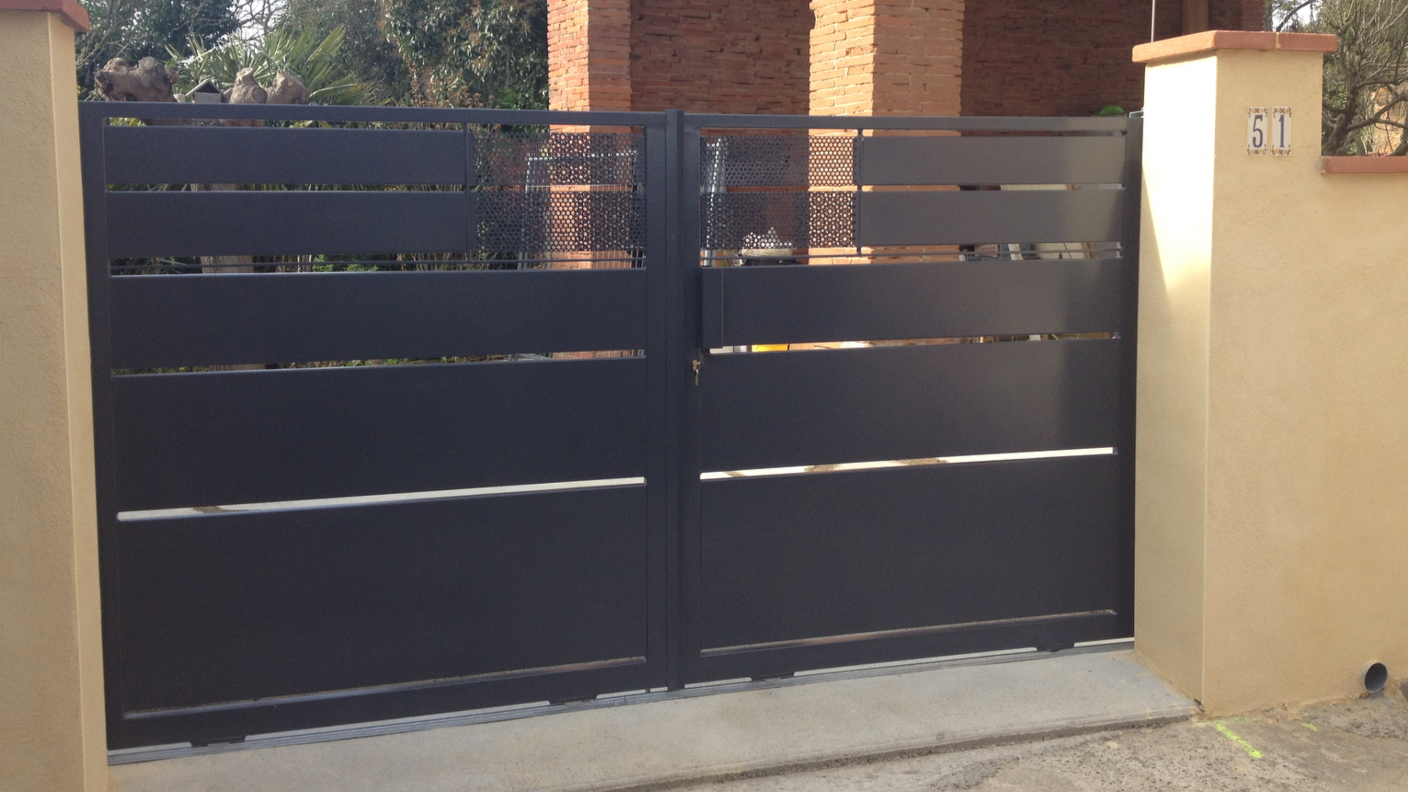 Portail métallique fermé, portes grises. Bâtiment en briques rouges en arrière-plan.