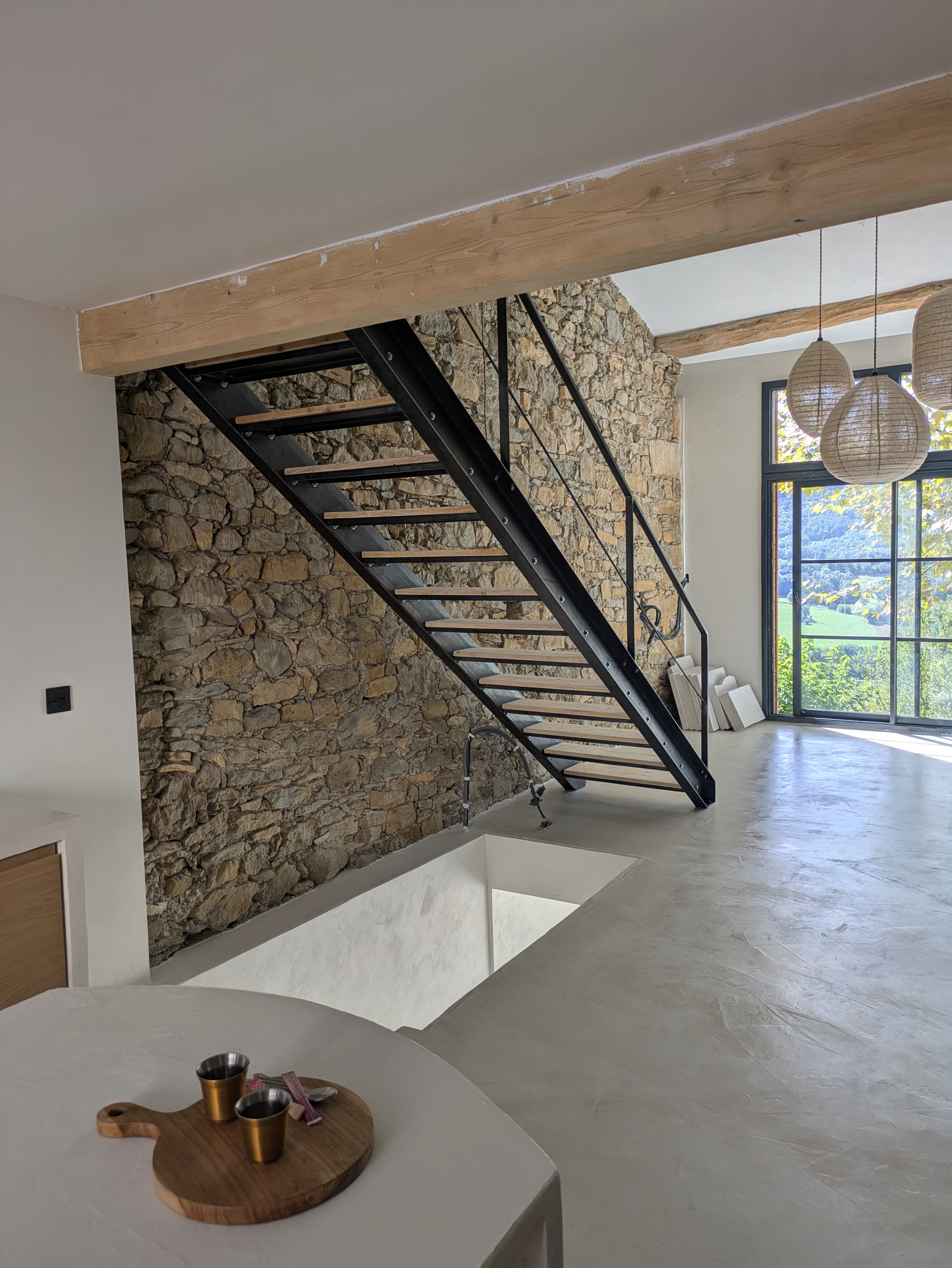 Escalier en métal noir, mur en pierre, intérieur moderne, bois clair, vue extérieure.