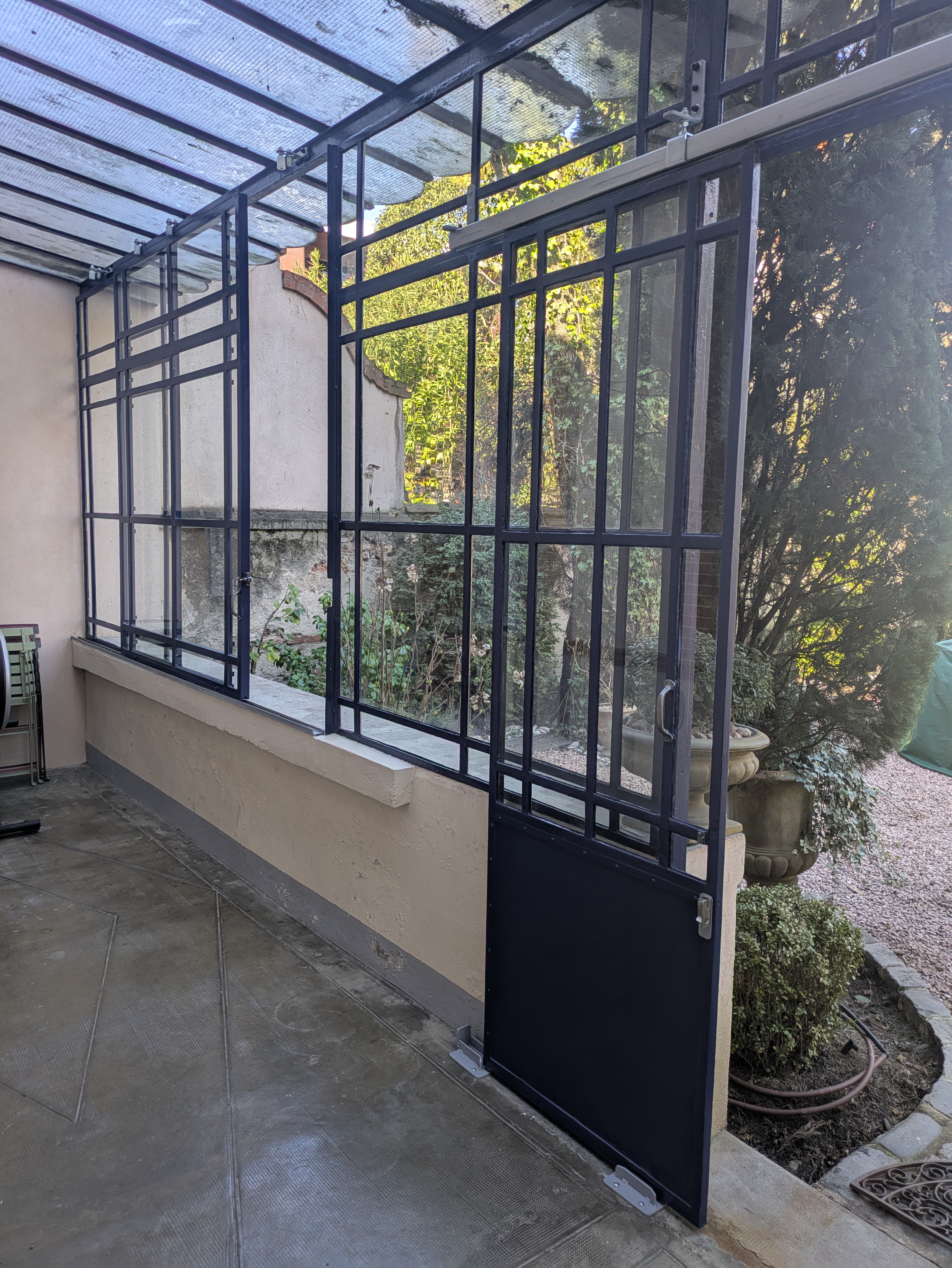 Une verrière noire avec porte ouverte et un jardin en arrière-plan.