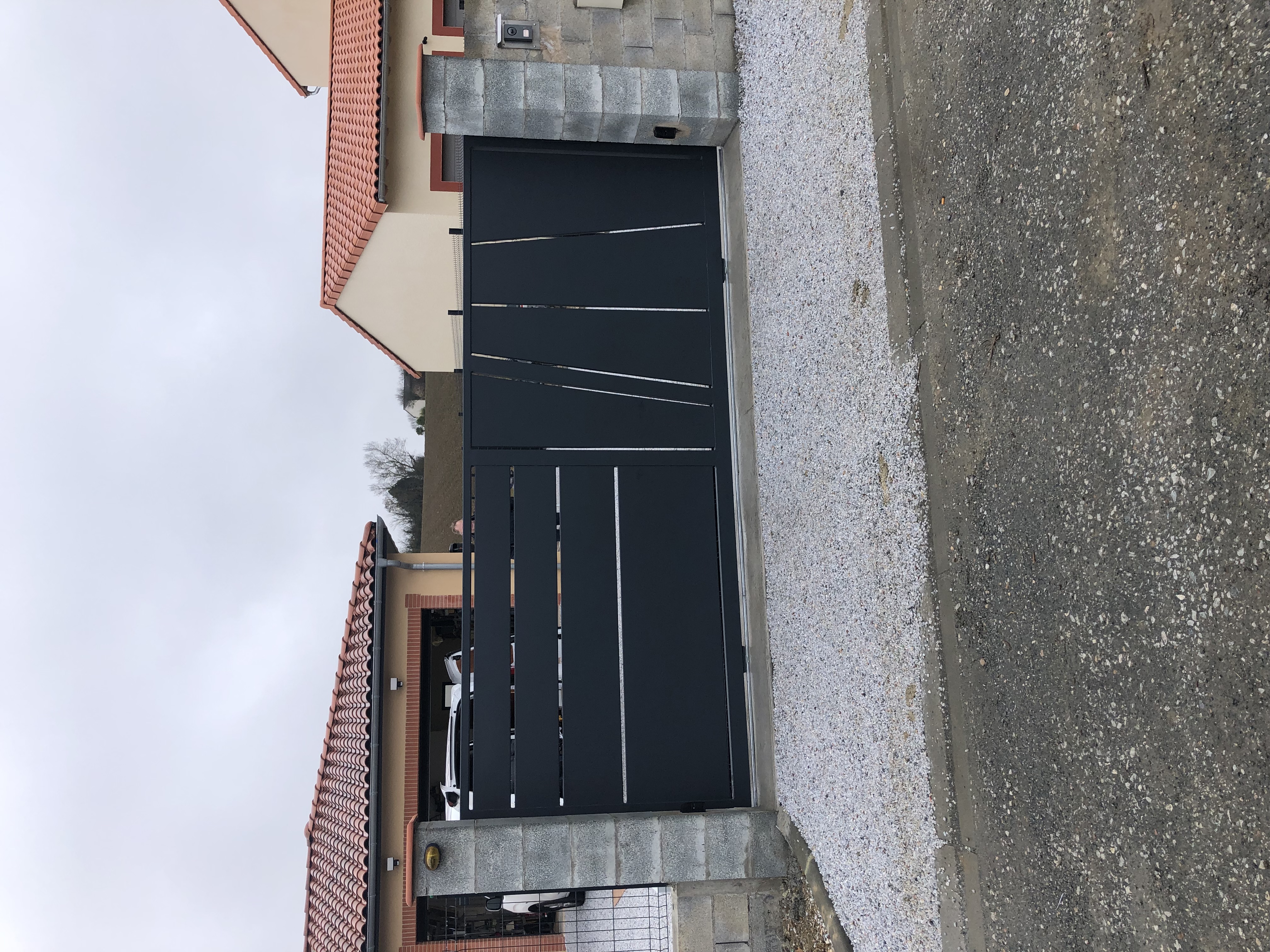 Grand portail gris avec des lignes décoratives devant une maison. Portail