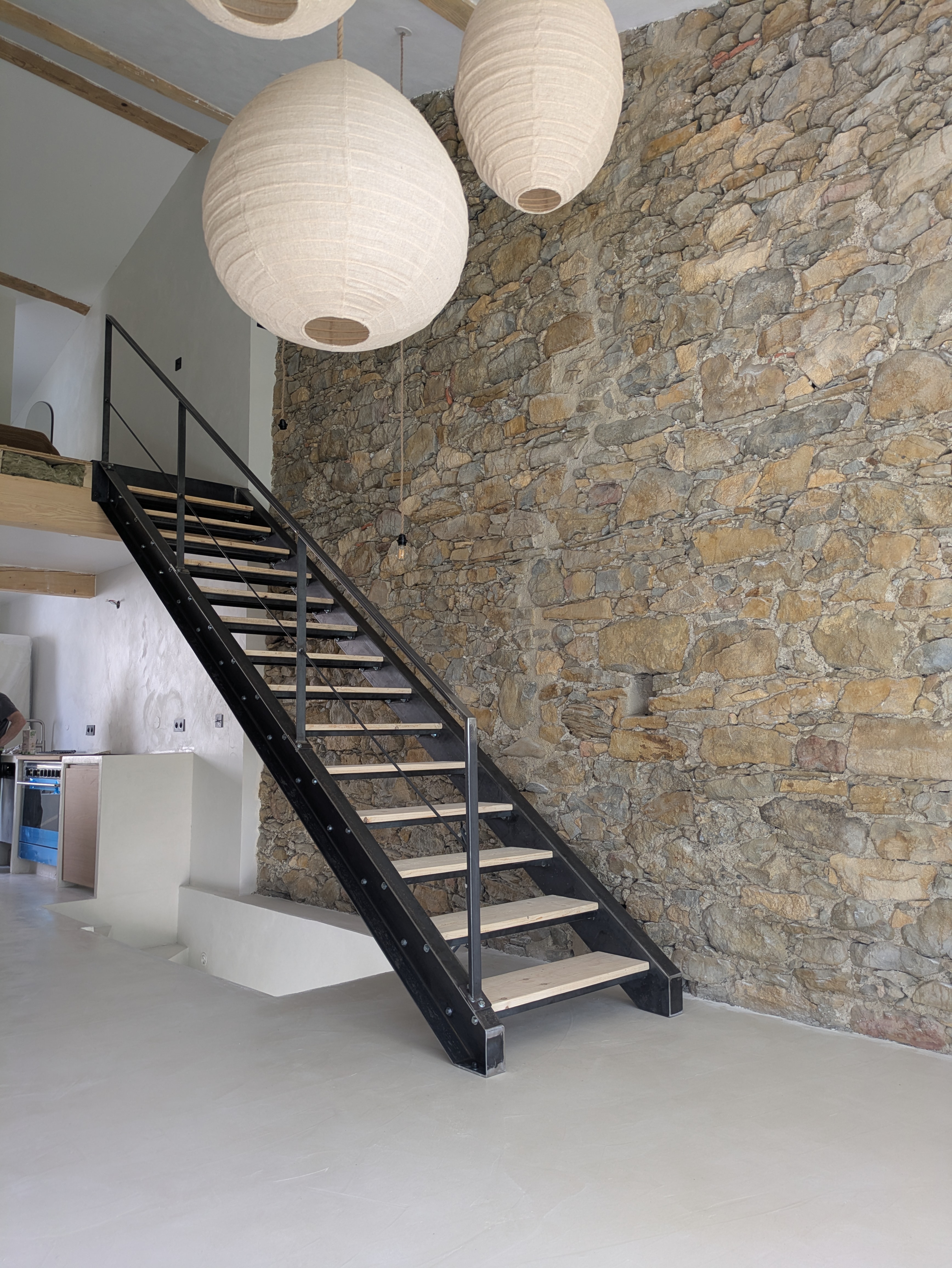 Escalier en métal noir avec de grandes lampes suspendues et mur en pierre.