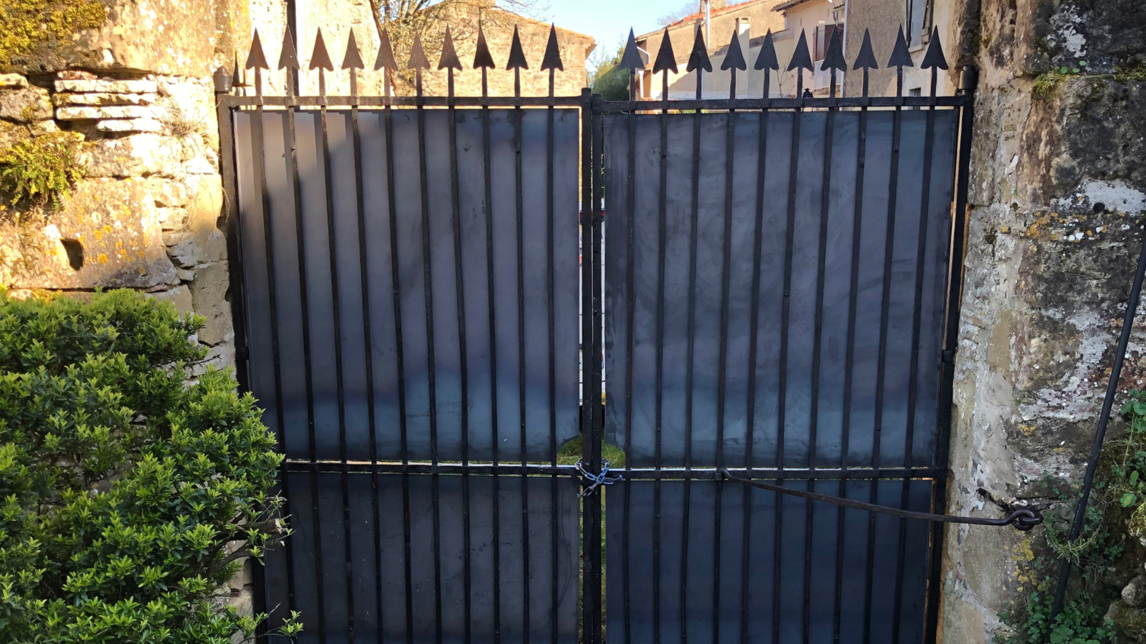 Grandes portes noires en fer forgé gardant l'entrée. Portail devant vieux murs.