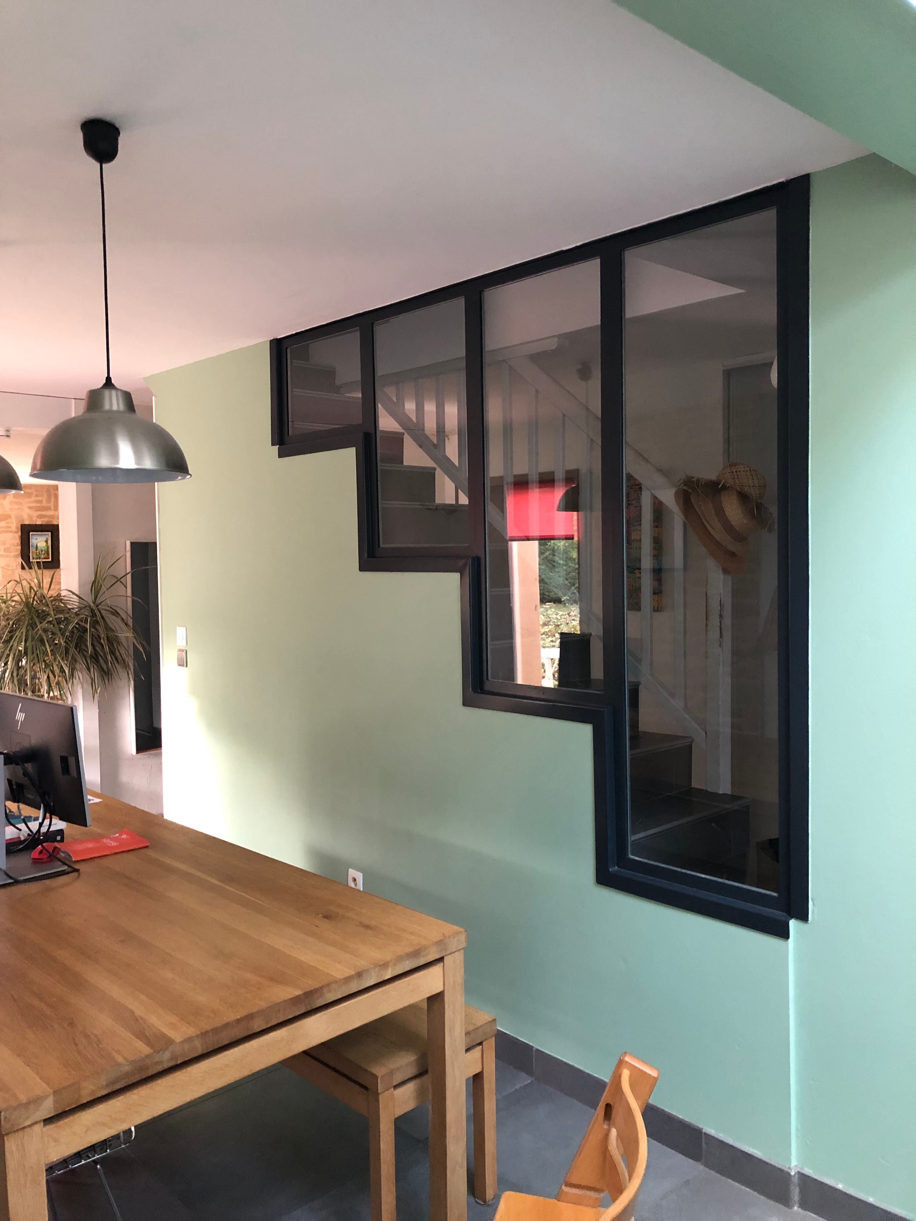 Intérieur avec escalier visible, table en bois et fenêtres, avec Verrière et un chapeau.