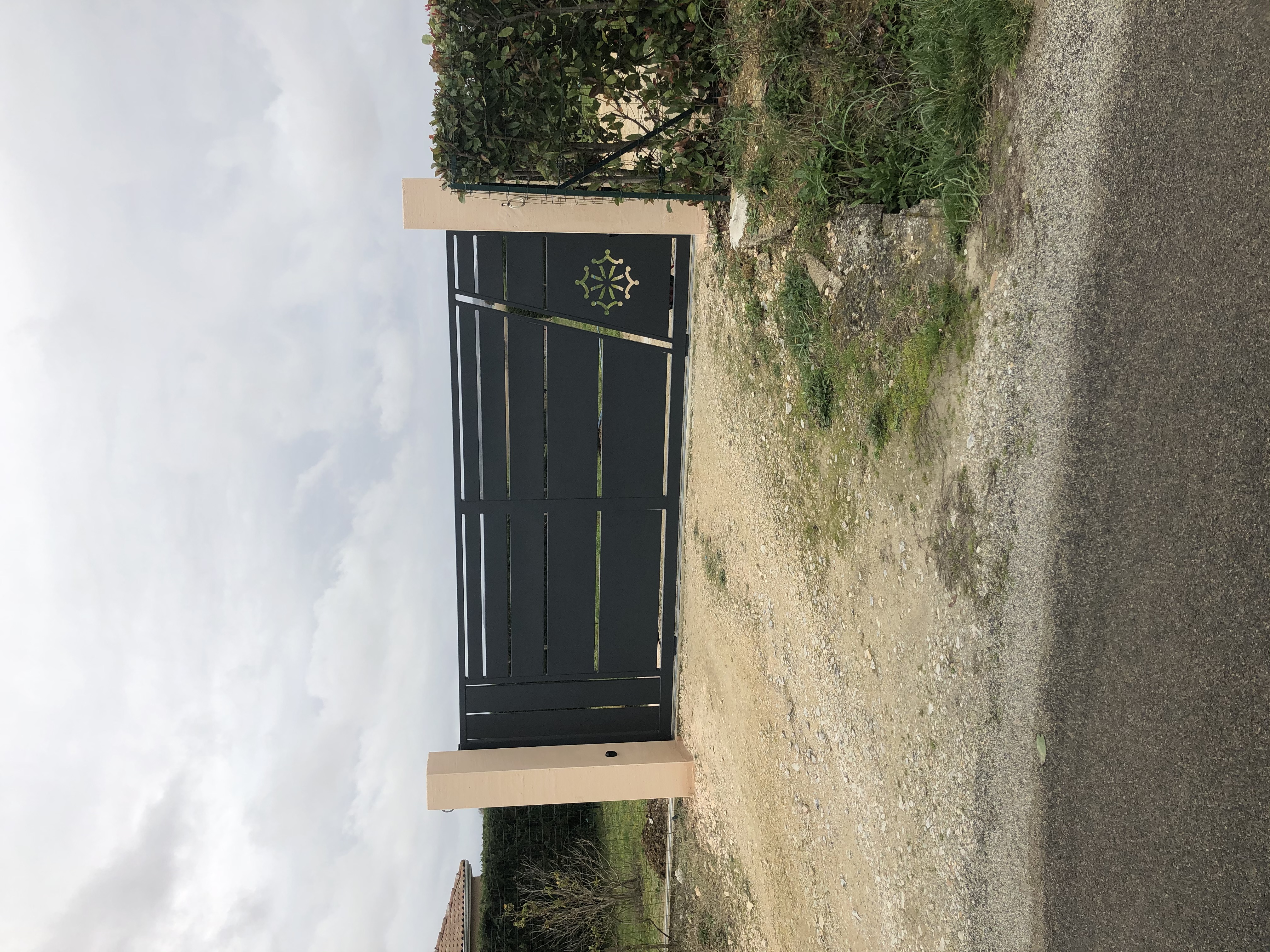 Grand portail noir fermé devant une maison, avec des piliers, et Christo