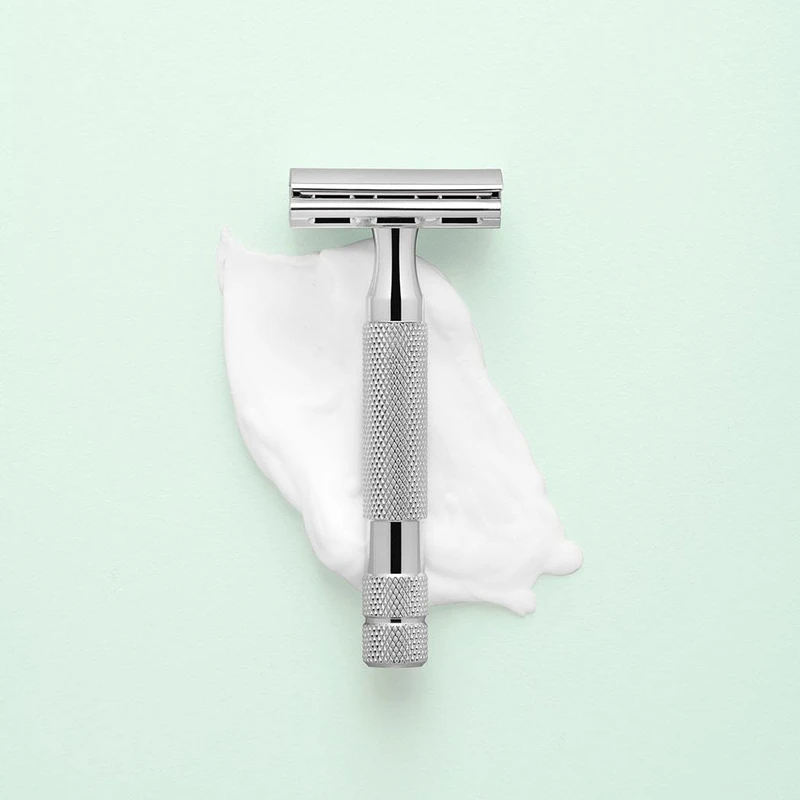 Metal safety razor placed on top of white shaving cream