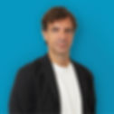 A man wearing a black suit jacket over a white shirt on a blue background.