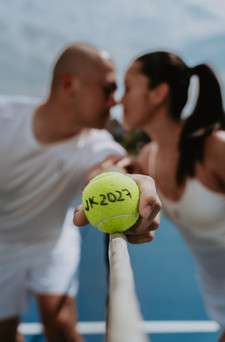 Close-up of a couple holding a yellow tennis ball marked with a date together between their faces
