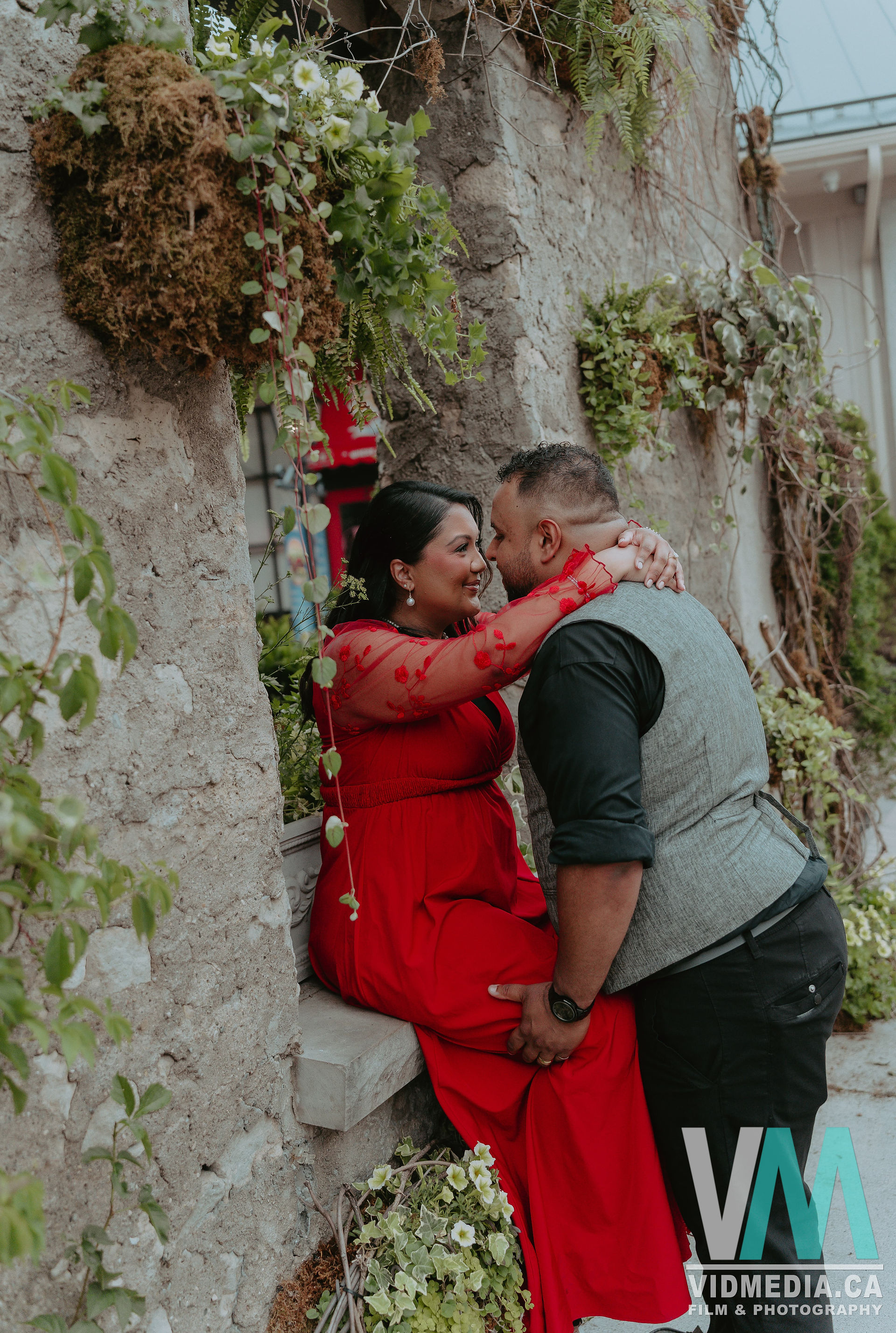 Couple hugging against an ivy-covered stone wall at Elora Mill.