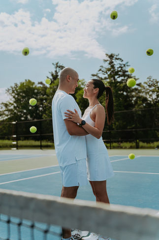 A couple embracing and smiling on a tennis court with yellow tennis balls scattered on the ground around them