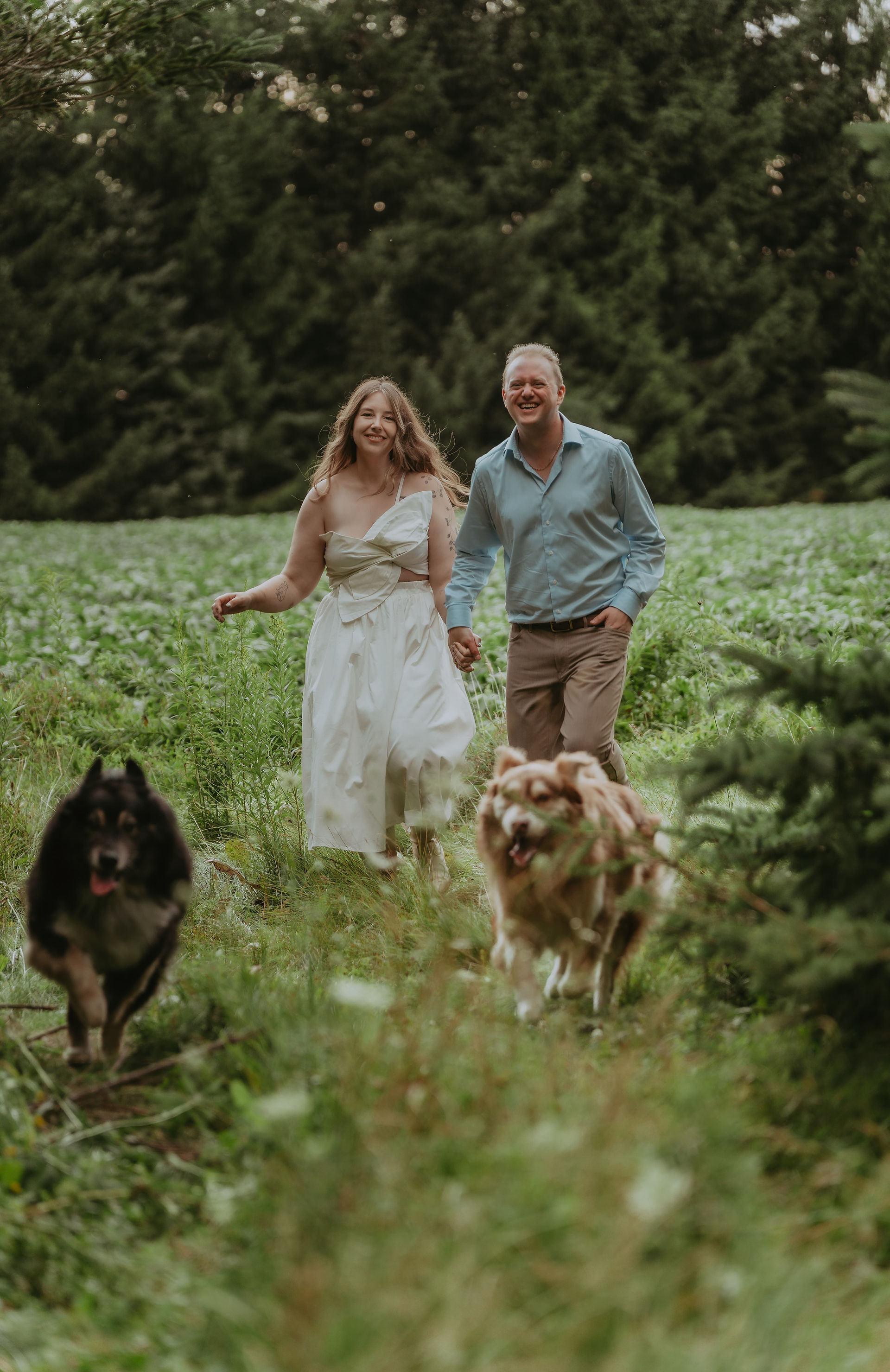 Candid engagement prompt showing couple running hand-in-hand through open fields.