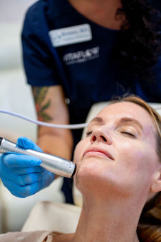 Woman receiving facial treatment from Vitaflow Wellness employee.