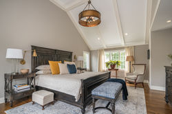 Master bedroom with wood bed frame, vaulted, beamed ceiling and round chandelier.